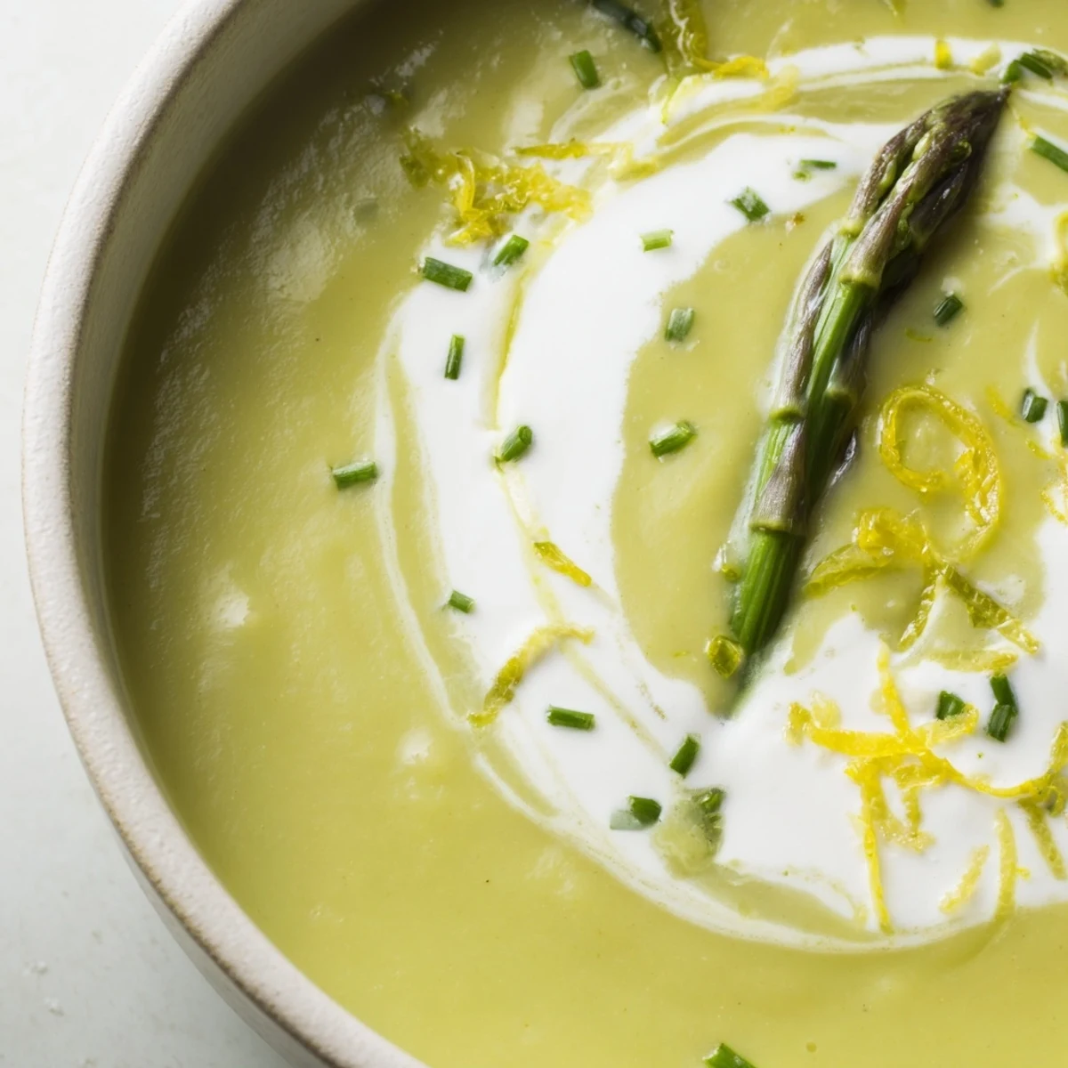 A vibrant swirl of crème fraîche tops this velvety, bright green spring soup, steaming gently.