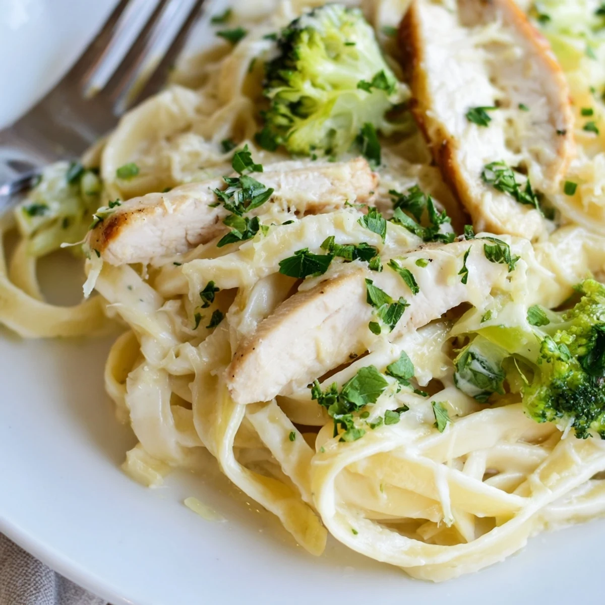 Steaming skillet of Creamy Chicken Alfredo with Broccoli tossed in silky Parmesan sauce garnished with parsley.