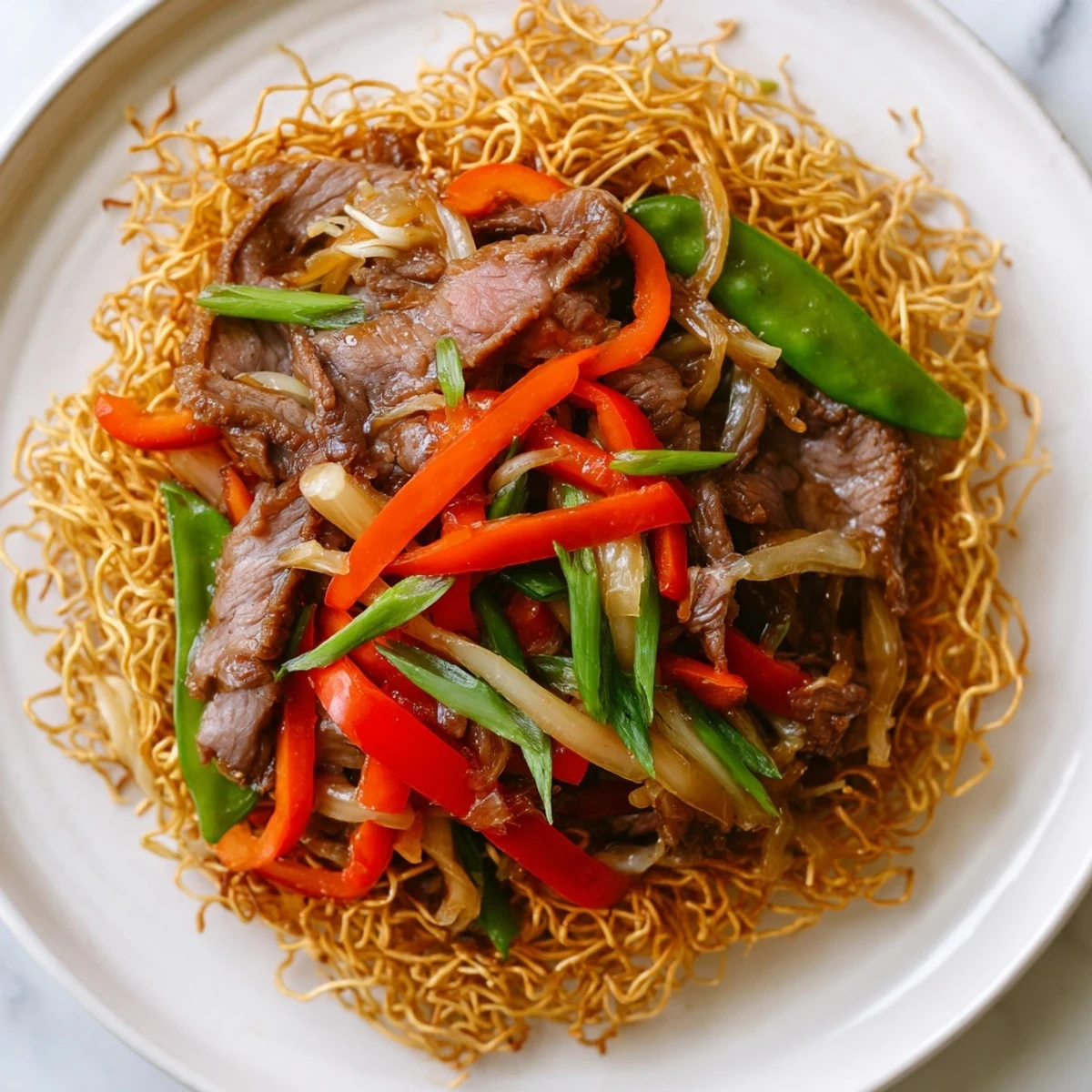 A close-up of golden crispy noodles laden with marinated beef, red peppers, and carrots.