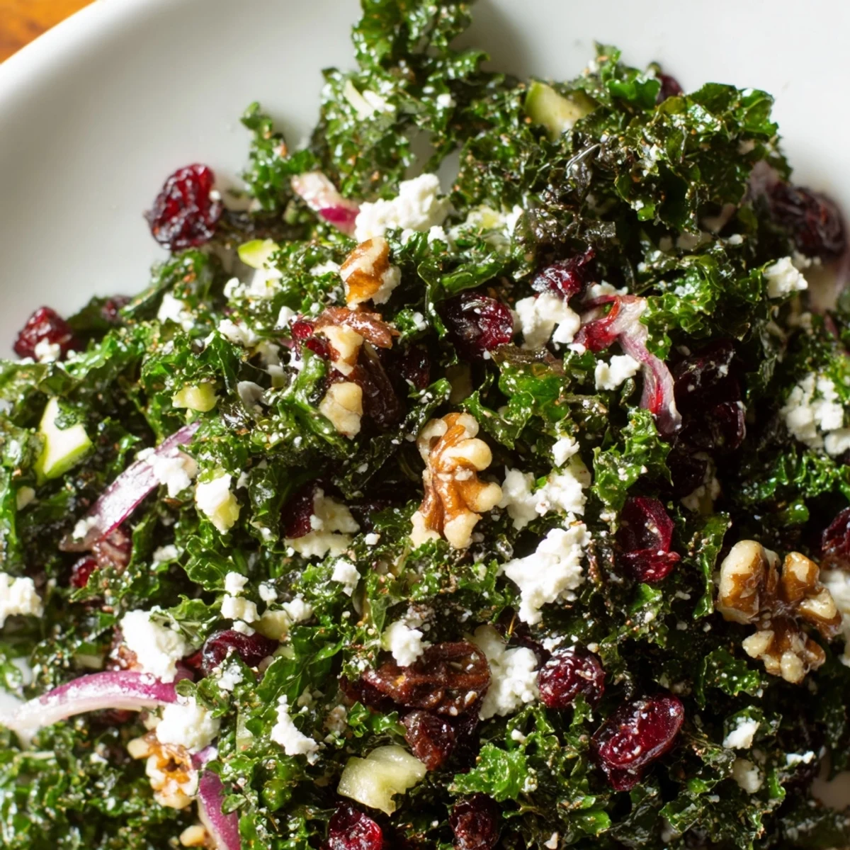 Close-up of Winter Kale Salad with Cranberries showing massaged kale leaves, red onion slices, and crunchy toasted walnuts.