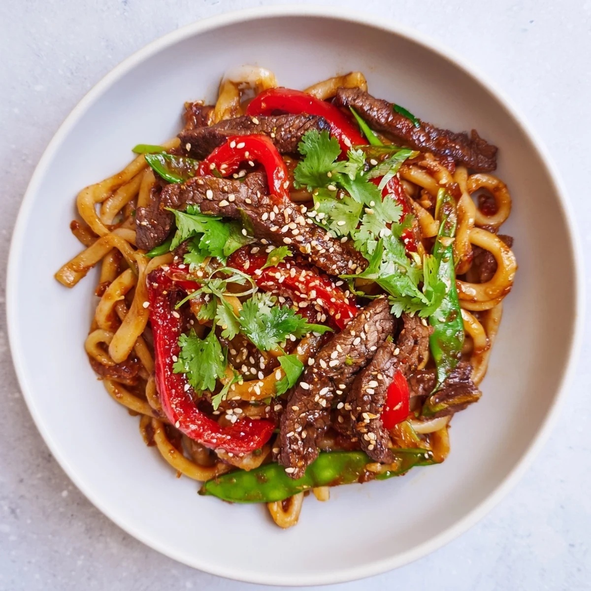 Colorful serving bowl of Spicy Beef Stir Fry with Udon Noodles, garnished with fresh cilantro and sesame seeds, ready to be enjoyed with chopsticks on a busy weeknight.