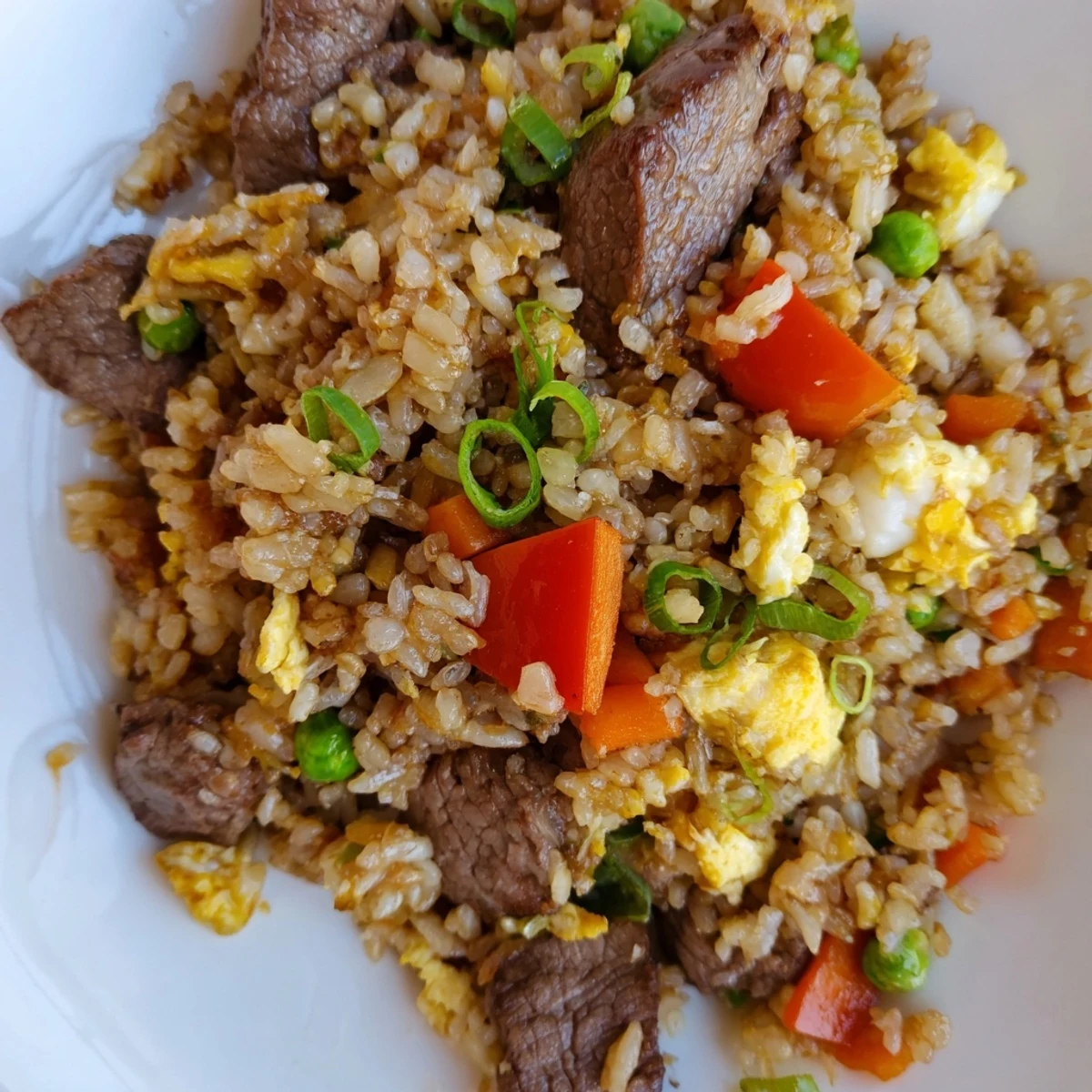 A close-up of Beef Fried Rice with Vegetables reveals crispy-edged beef, sweet peas, and scrambled egg ribbons tossed with savory sauce.