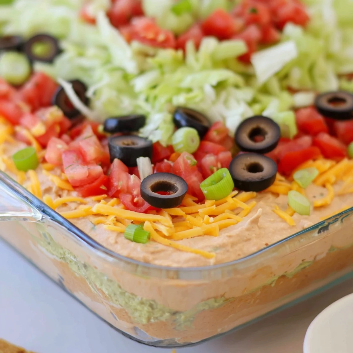 Seven Layer Taco Dip with chips showcases colorful layers of beans, guacamole, and cheese served chilled for game day.  