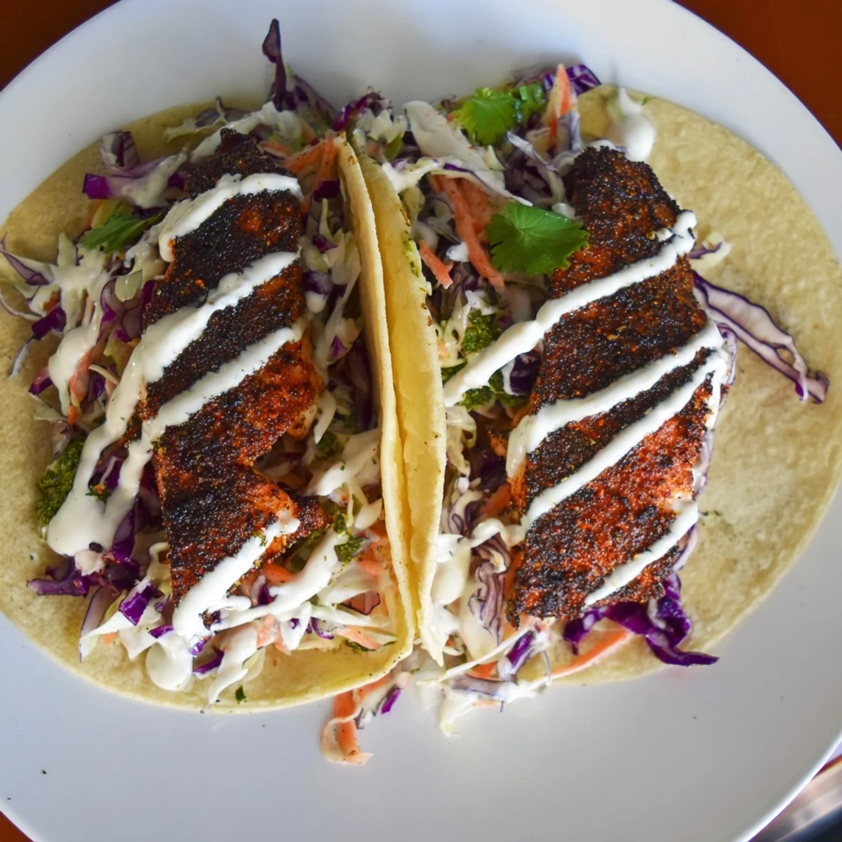 Assembled Louisiana Blackened Fish Tacos overflowing with flaky fish, tangy slaw, and creamy sauce on a rustic plate.