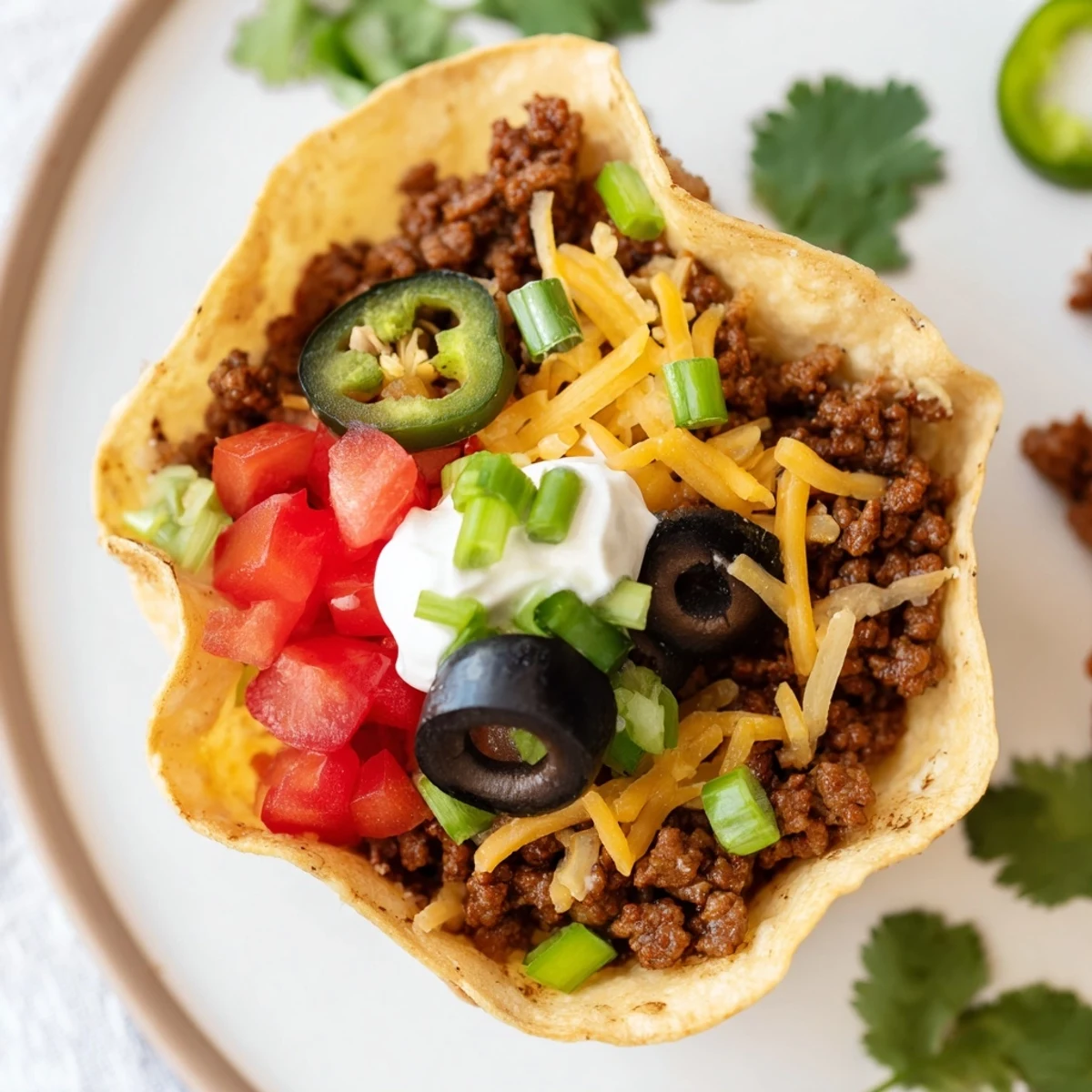Golden-brown tortilla cups filled with seasoned ground beef and melted cheddar, topped with sour cream and fresh cilantro for a savory game day bite.
