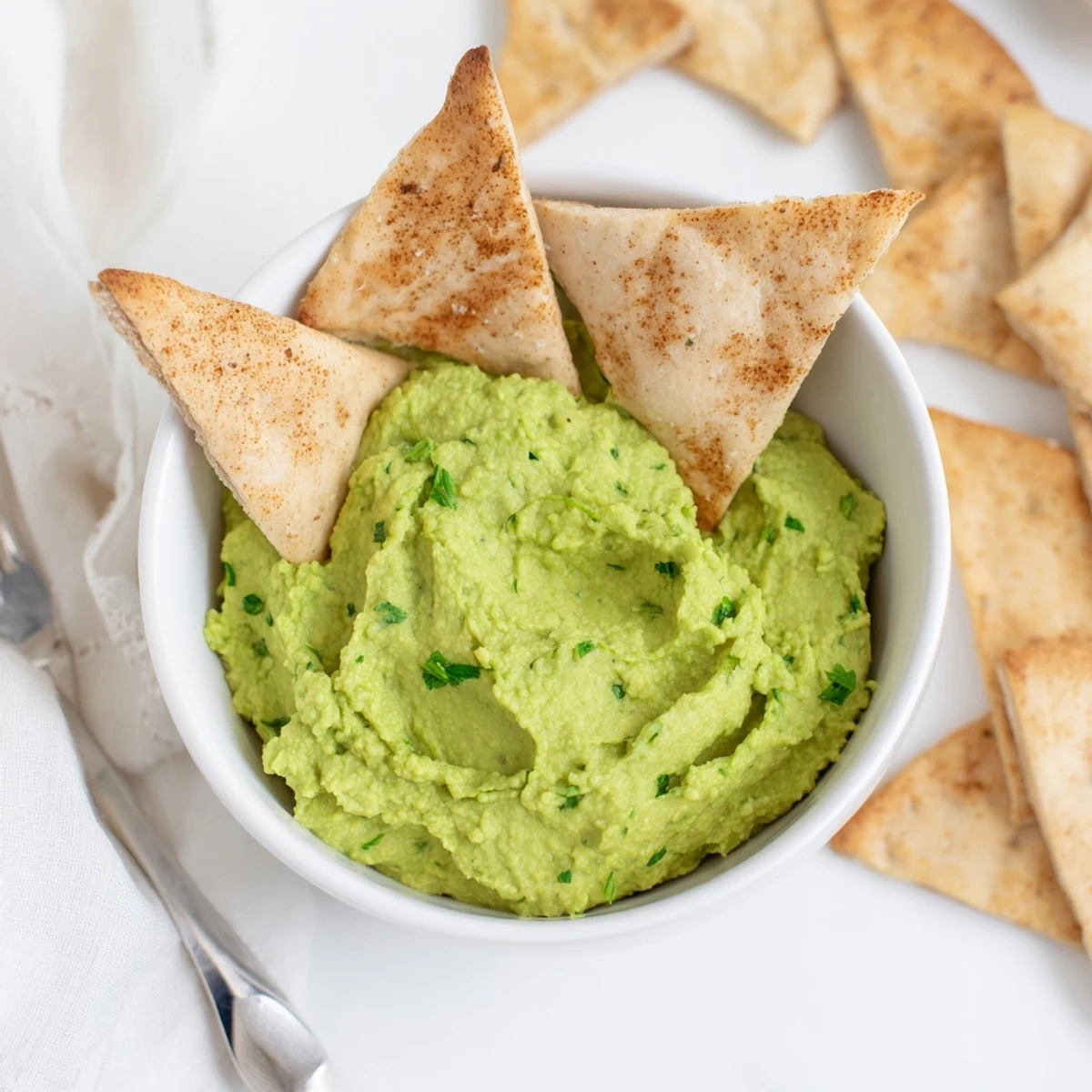 A close-up of vibrant Green Avocado Hummus, creamy and green, served alongside golden, crispy baked pita triangles.