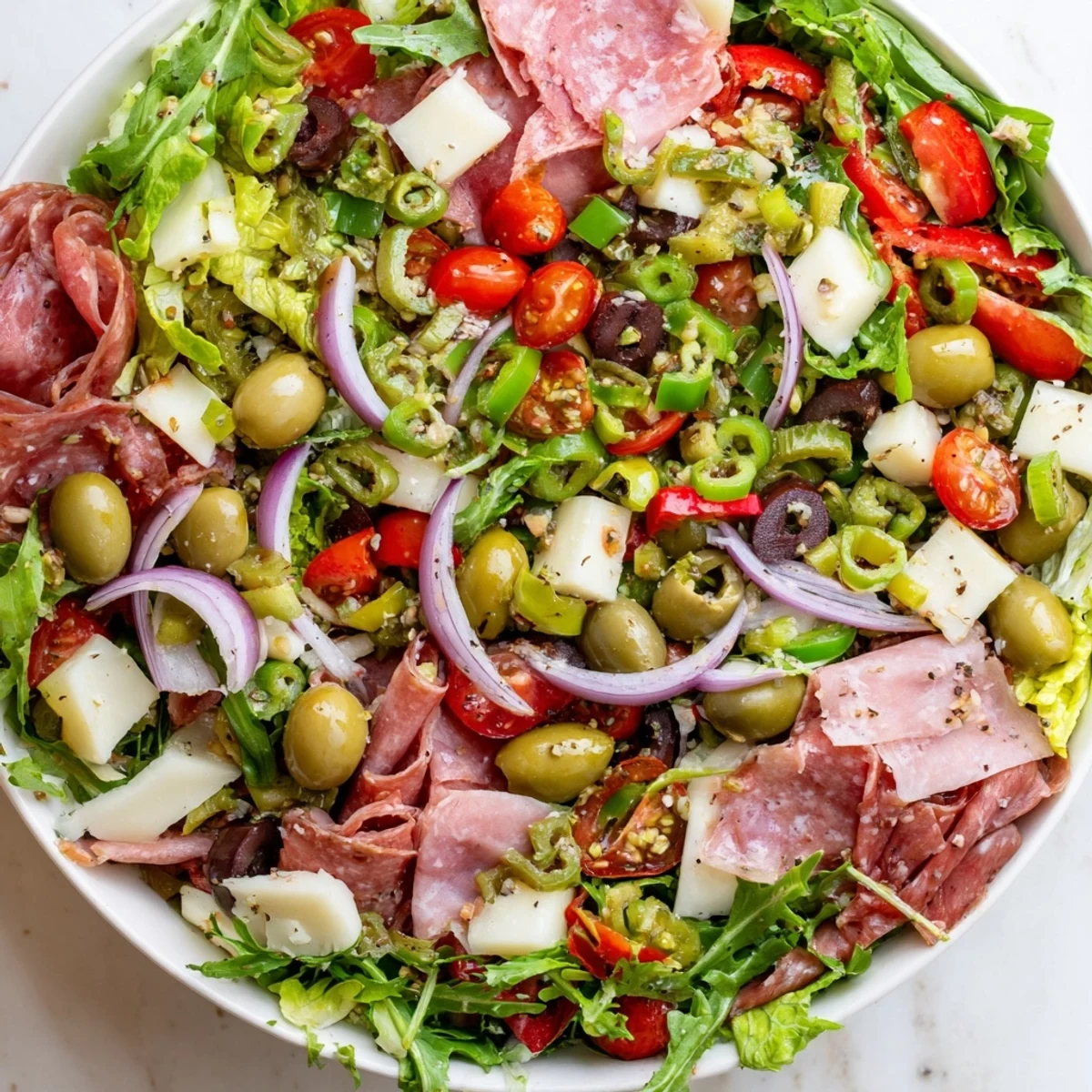 Fresh New Orleans Muffuletta Salad topped with green and Kalamata olives, cured meats, provolone, and mozzarella on a bed of greens.