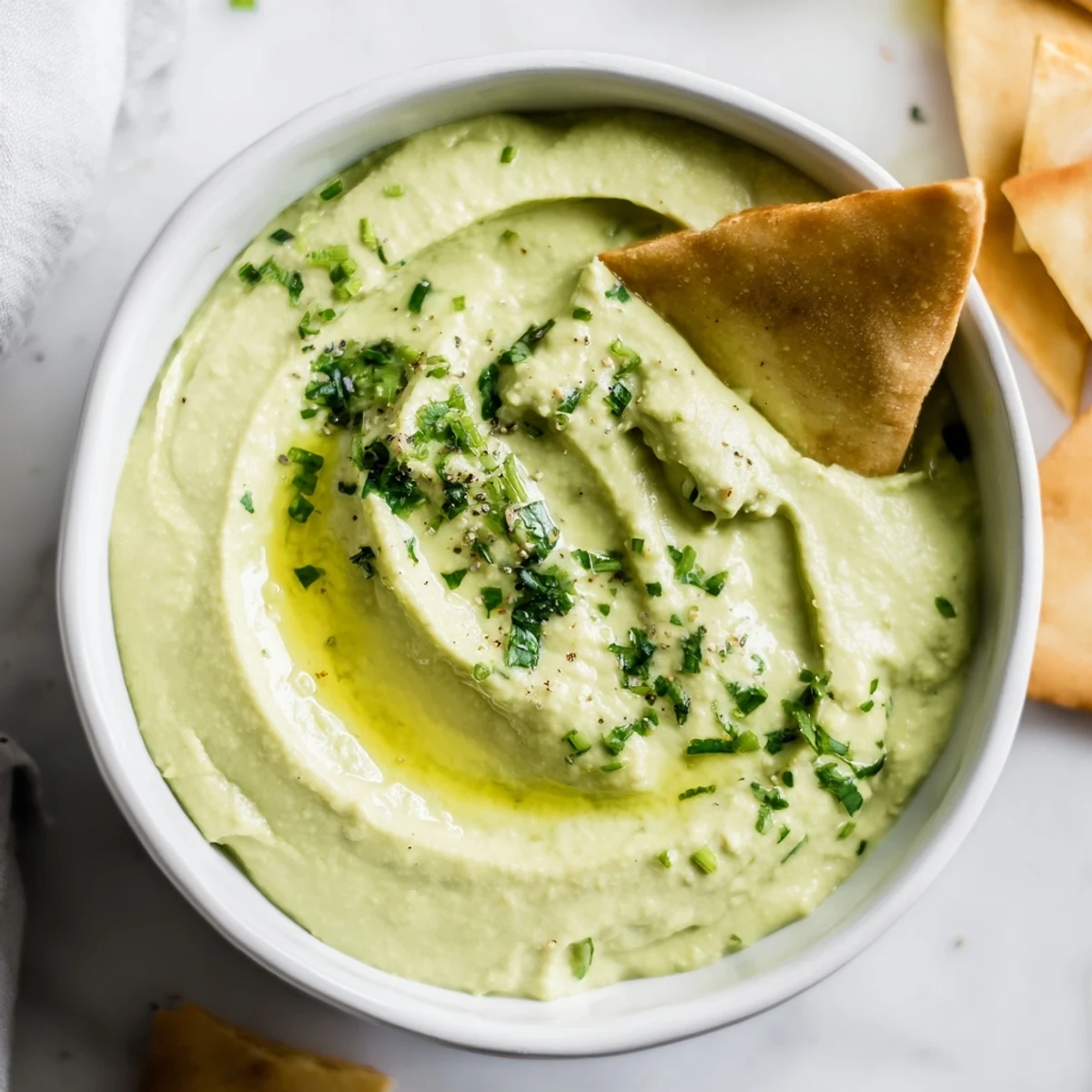 Creamy, herb-filled Green Avocado Hummus garnished with fresh cilantro and chives, paired with crisp pita triangles on a wooden board.  