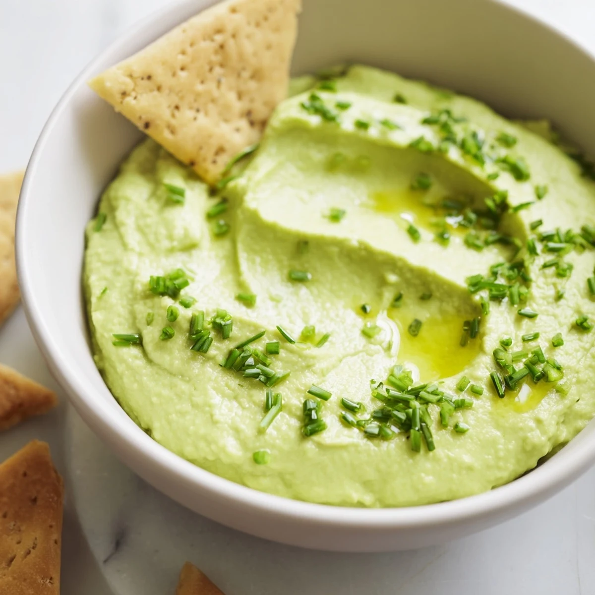 Ready-to-serve Green Avocado Hummus with a drizzle of olive oil, surrounded by crunchy pita chips on a rustic platter.