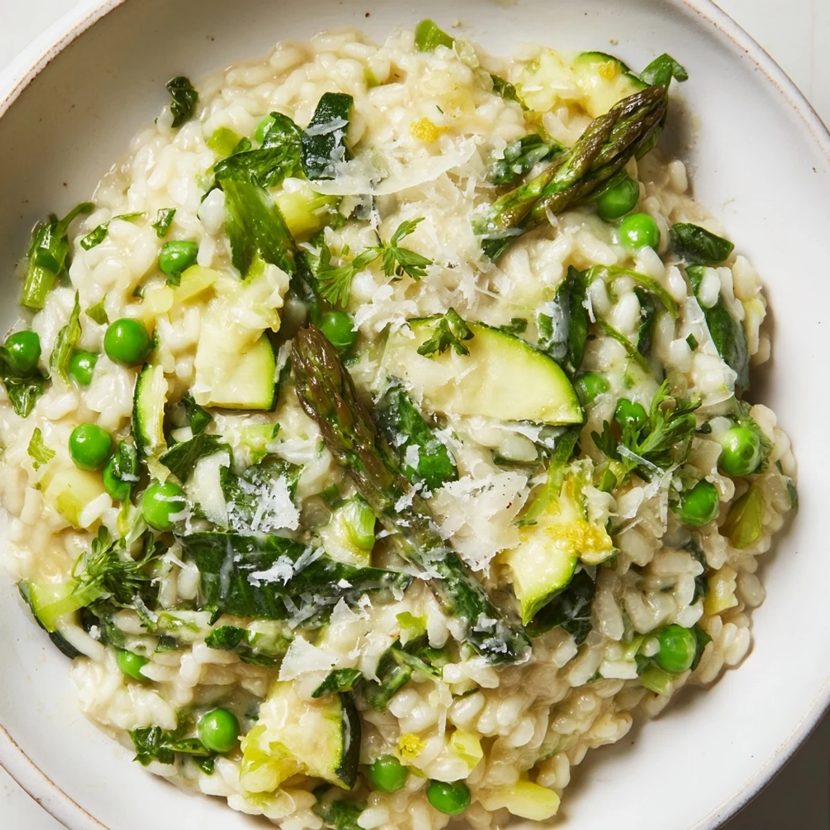 A close-up of Spring Vegetable Risotto, highlighting the steamy, tender zucchini and leek in a glossy, Parmesan-flecked sauce.
