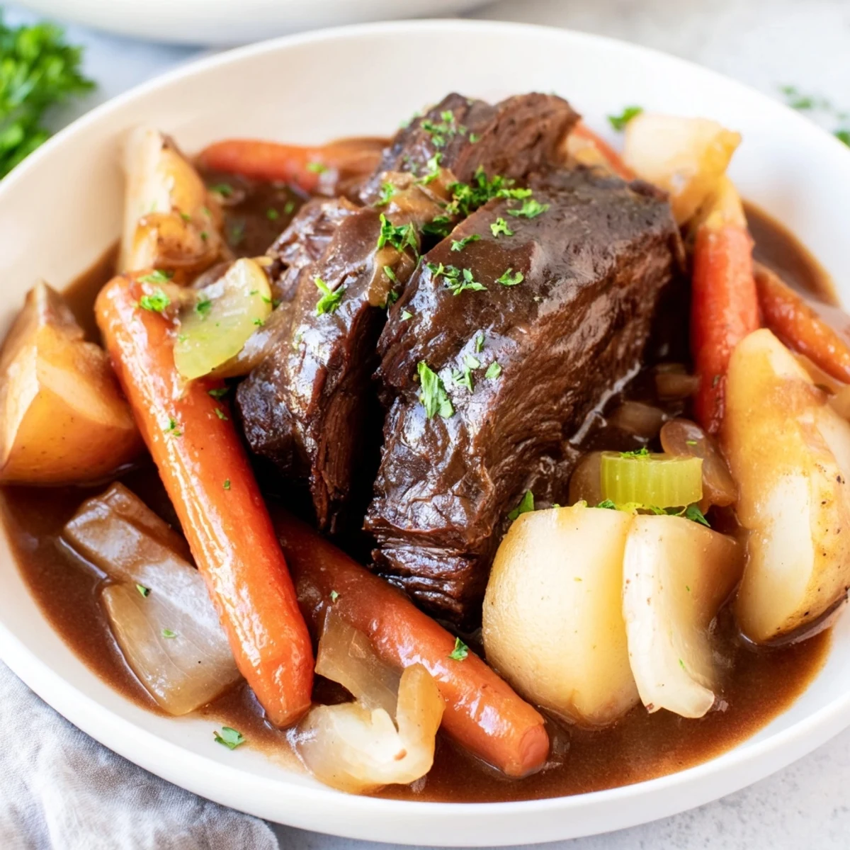 Slow Cooker Beef Pot Roast with Root Veggies sits in a ceramic dish with caramelized carrots, potatoes, and onions glistening with rich gravy, garnished with fresh parsley.