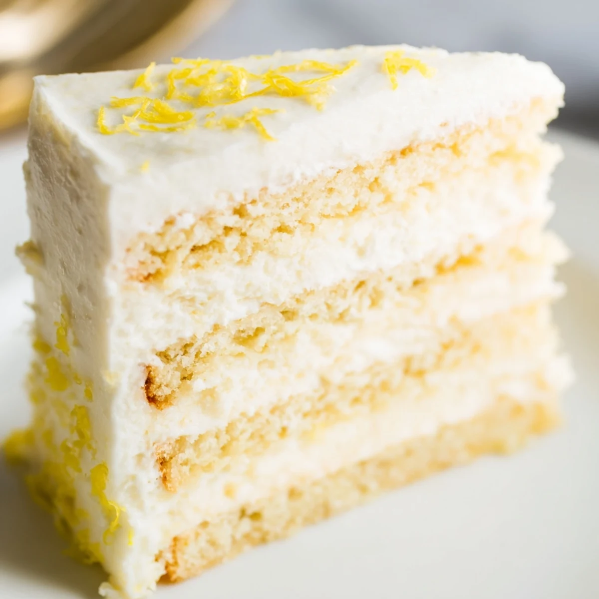 Golden layers of Limoncello Mascarpone Cake sit on a marble counter, with lemon zest and white chocolate curls garnishing the top.
