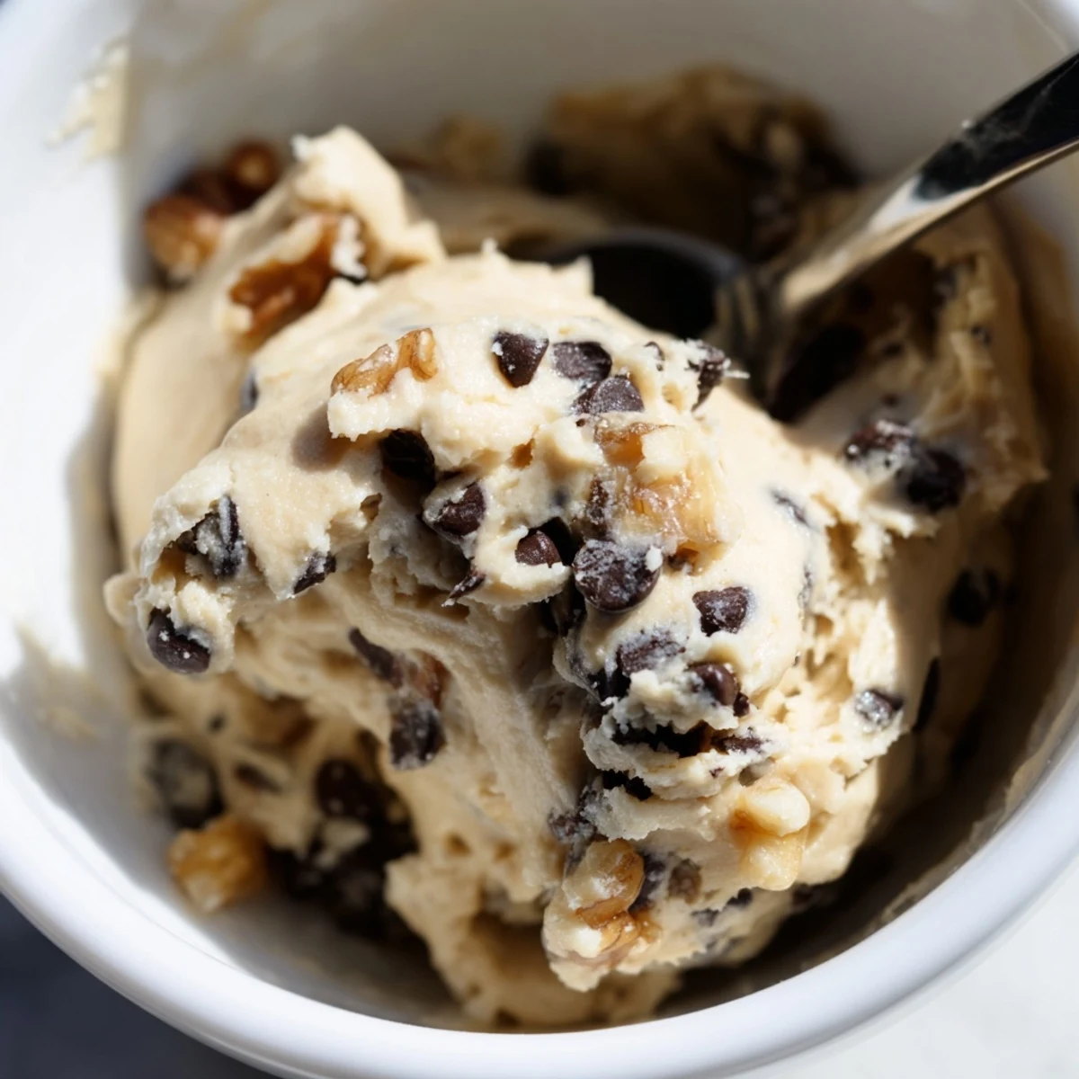 A spoonful of Guilt Free Greek Yogurt Cookie Dough showcases creamy texture with mini dark chocolate chips and chopped walnuts.