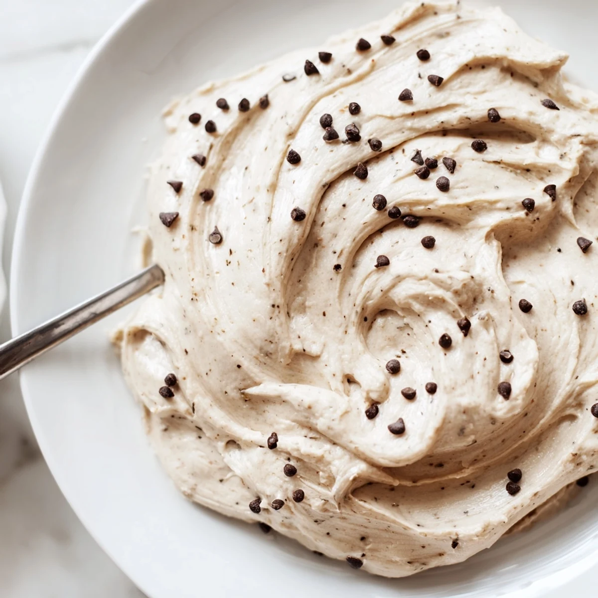 The creamy frosting in a bowl offers spoonfuls of edible cookie dough flavor, perfect for topping a batch of freshly baked cupcakes.