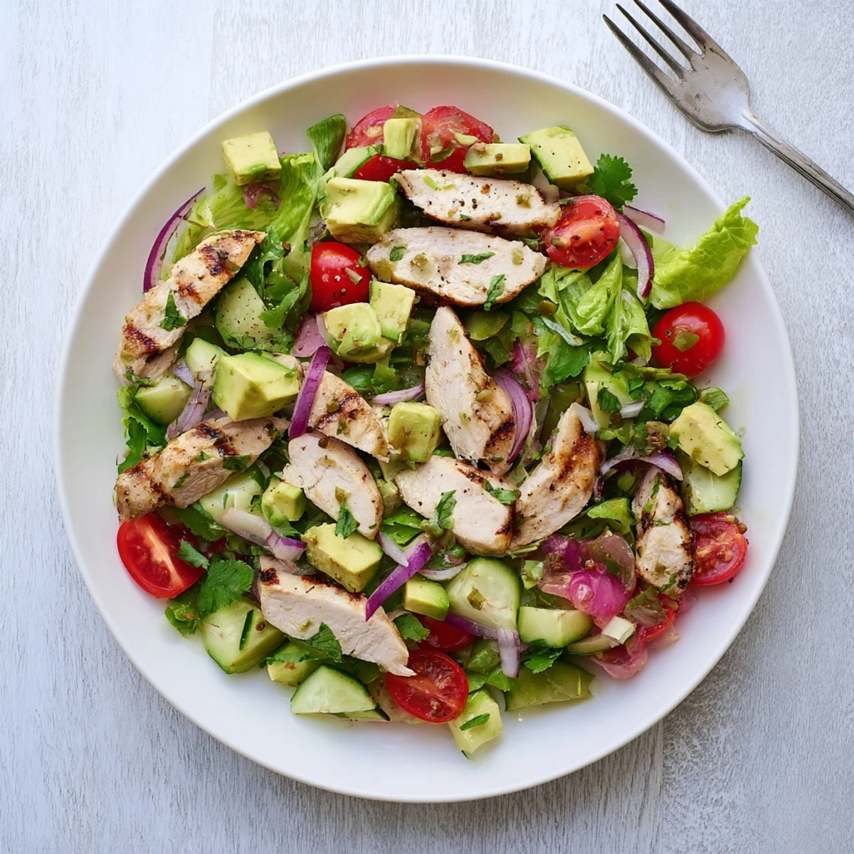 Freshly grilled chicken slices nestled with creamy avocado cubes and colorful veggies in Avocado Chicken Salad, served on a bed of mixed greens.