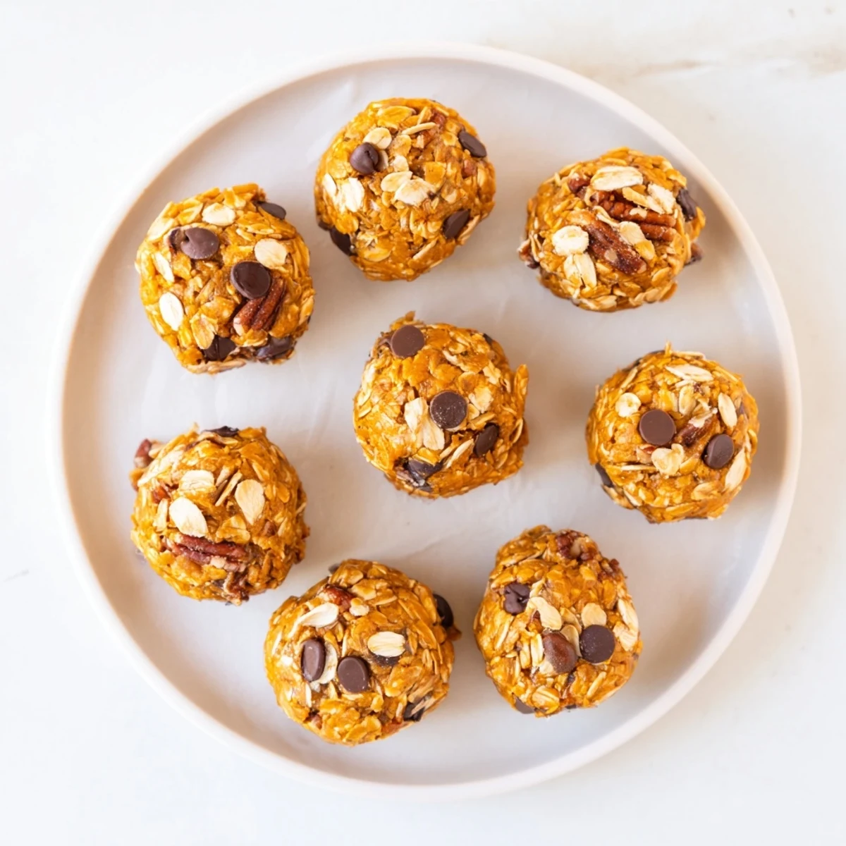 Perfectly rolled No Bake High Protein Pumpkin Bites featuring oats and maple syrup on a plate.