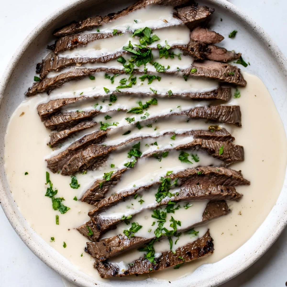Sliced flank steak drizzled with roasted garlic sauce, plated with fresh parsley and a side of green beans.