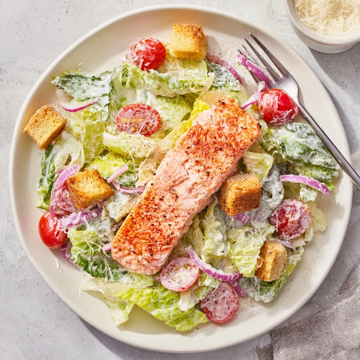 Fresh salmon fillet resting atop vibrant Caesar salad with cherry tomatoes, red onion, and Parmesan cheese
