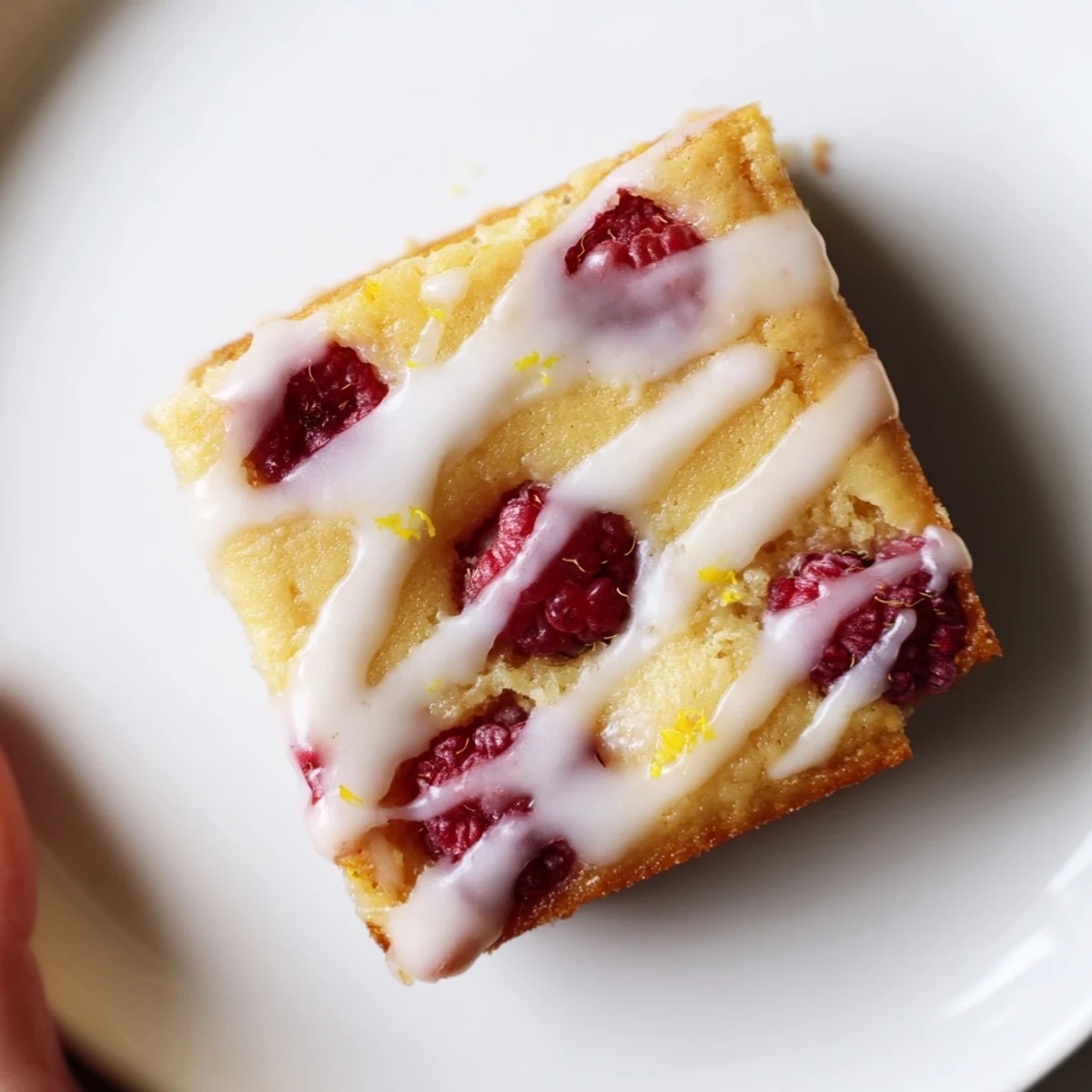 Square raspberry lemon blondies with tangy glaze and bright red berry pieces visible