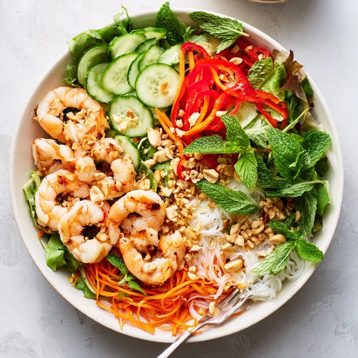 Fresh spring roll salad bowl featuring julienned vegetables, herbs, rice noodles, and succulent shrimp with zesty dressing