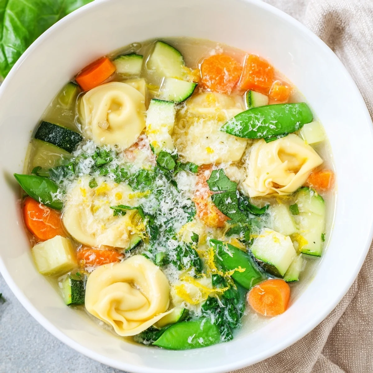 Golden bowl of spring tortellini soup garnished with lemon zest, Parmesan, and parsley