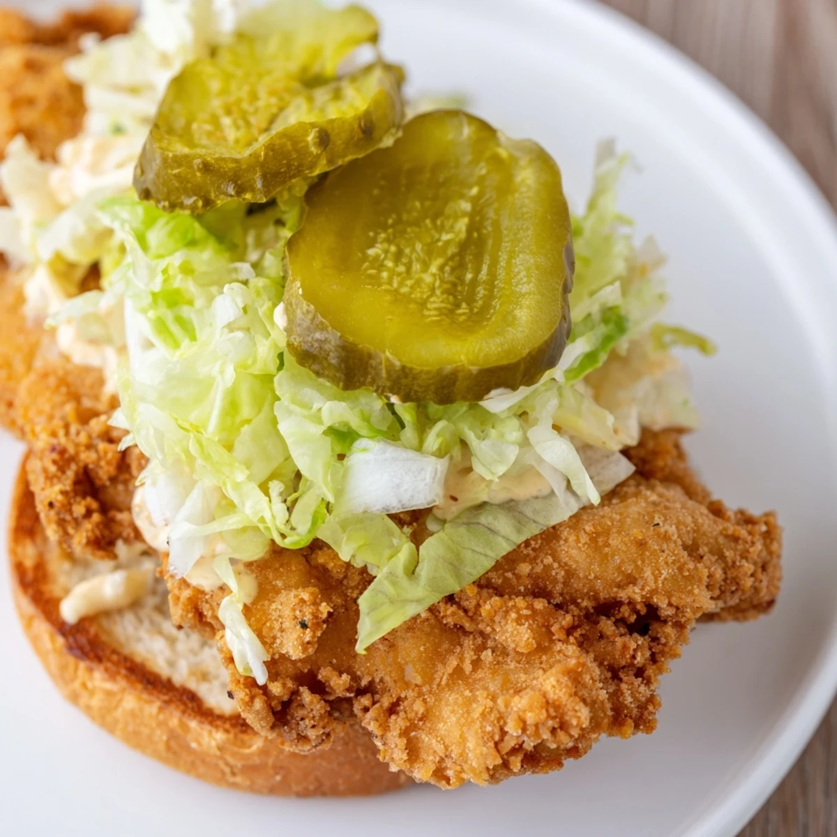 Fried chicken breast sandwich featuring crunchy coating creamy sauce and crisp vegetables on a soft bun