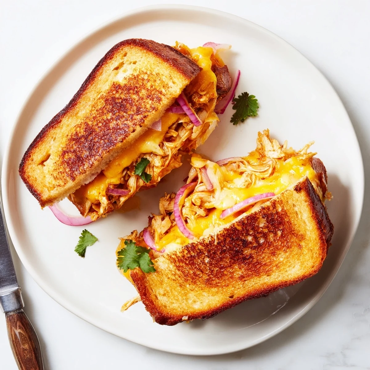 Warm sandwich stacked with tender barbecue chicken and melted cheese served on a wooden cutting board
