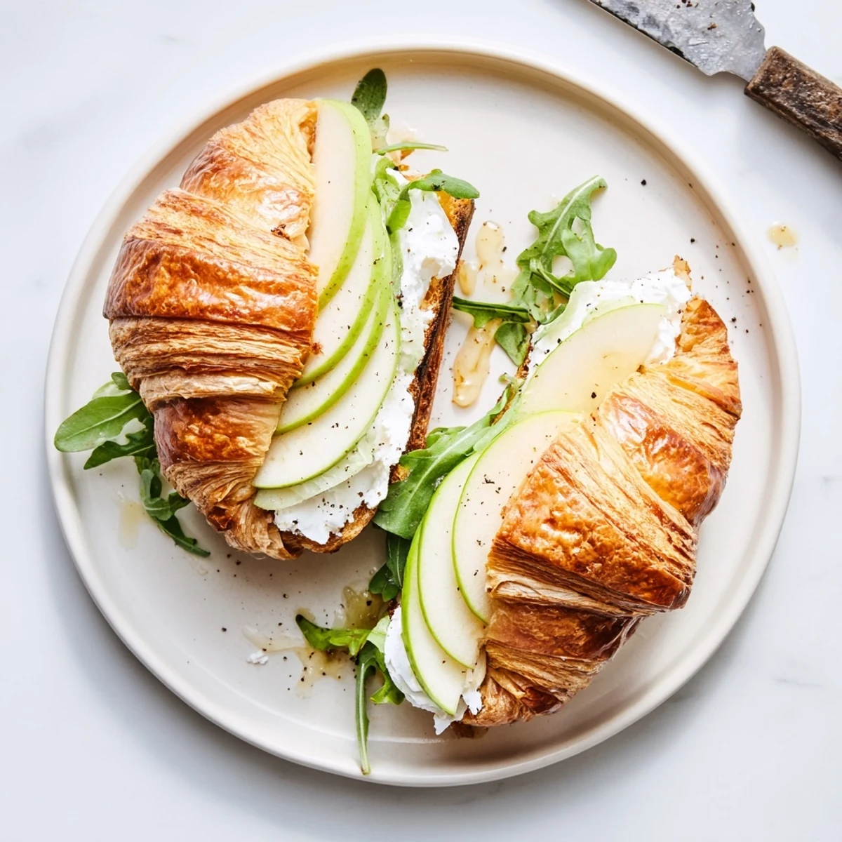 Flaky croissant sandwich layered with creamy goat cheese, crisp apple slices, and fresh peppery arugula