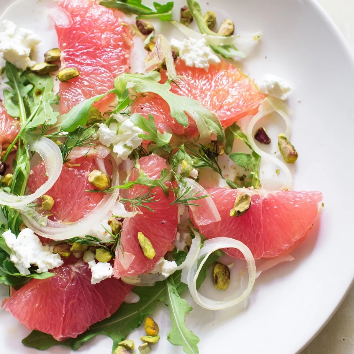 Grapefruit, goat cheese and fennel salad arranged on a white platter with pink citrus segments and green fennel fronds