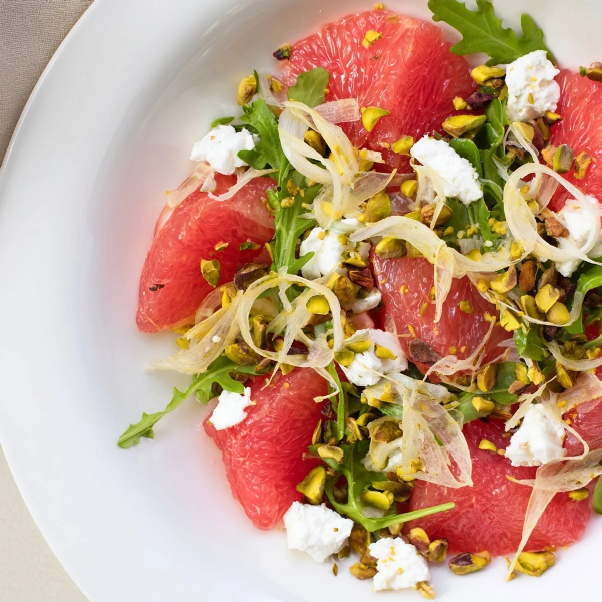 Fresh grapefruit goat cheese and fennel salad drizzled with dressing and topped with crumbled cheese and pistachios