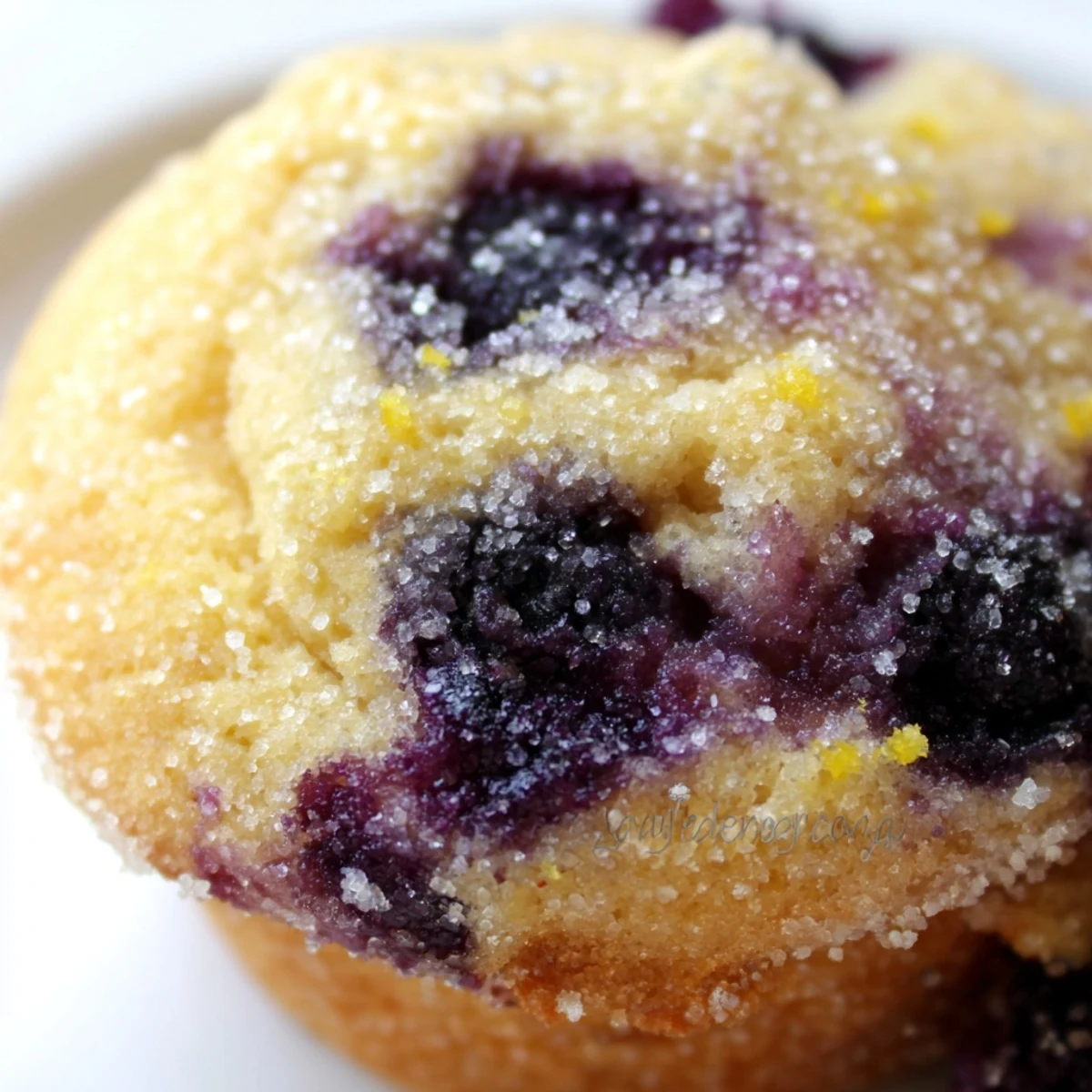 Golden lemon blueberry muffins topped with sparkling sugar on a rustic wooden board