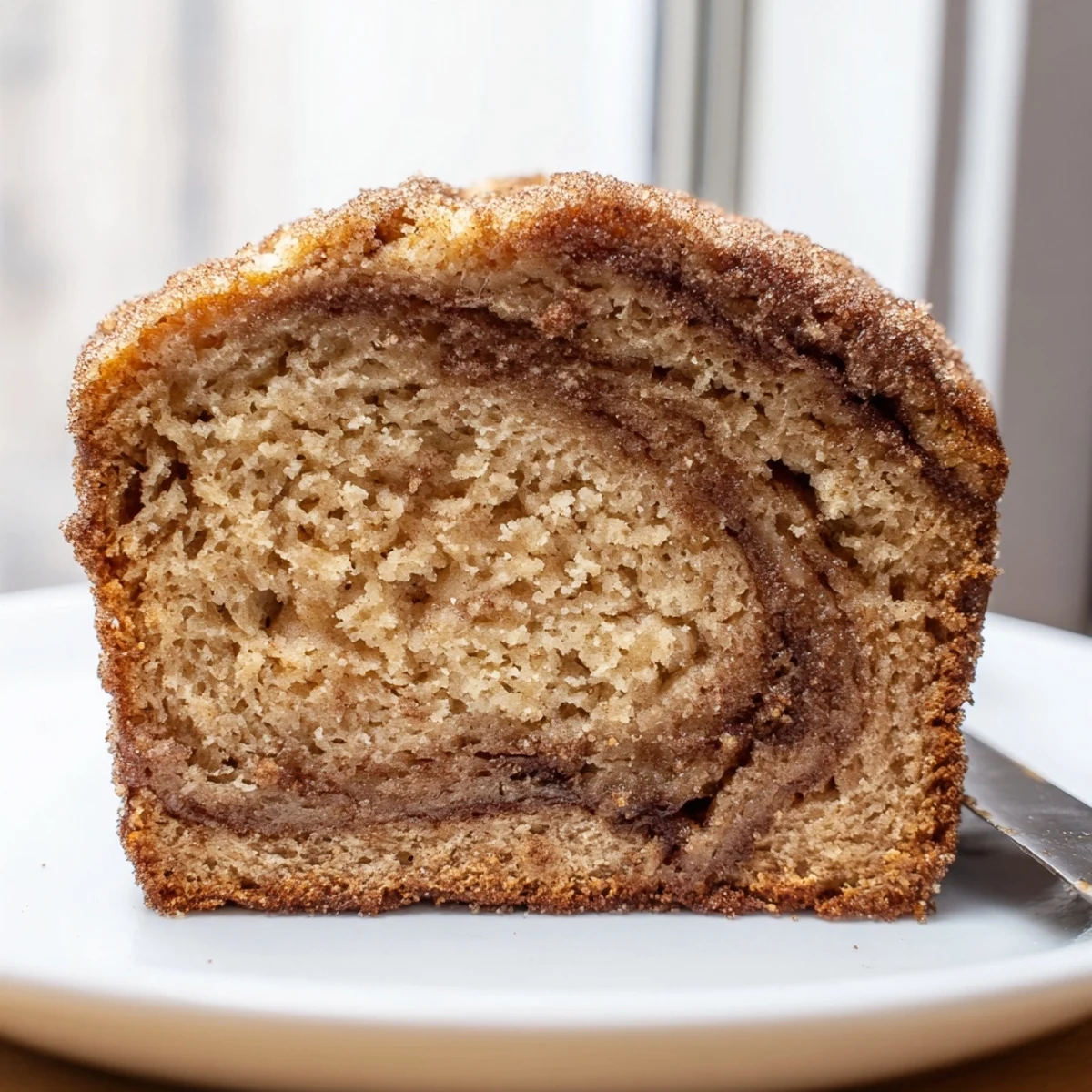 A thick slice of snickerdoodle banana bread drizzled with melted butter beside a steaming cup of coffee