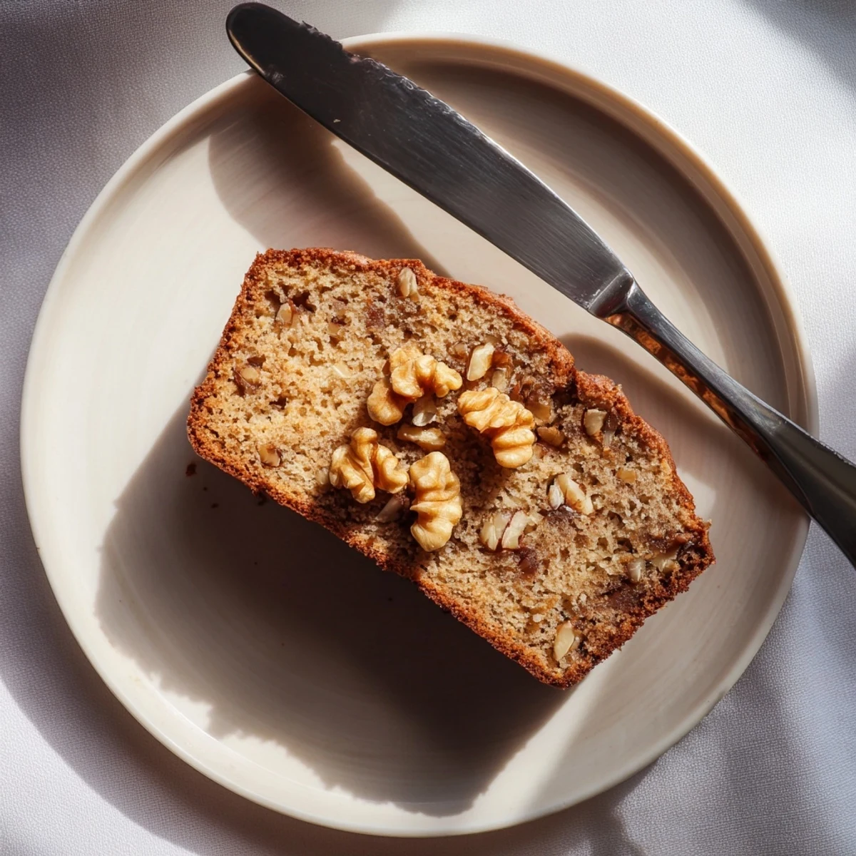 Golden banana nut bread loaf topped with crunchy walnuts on a rustic cutting board.