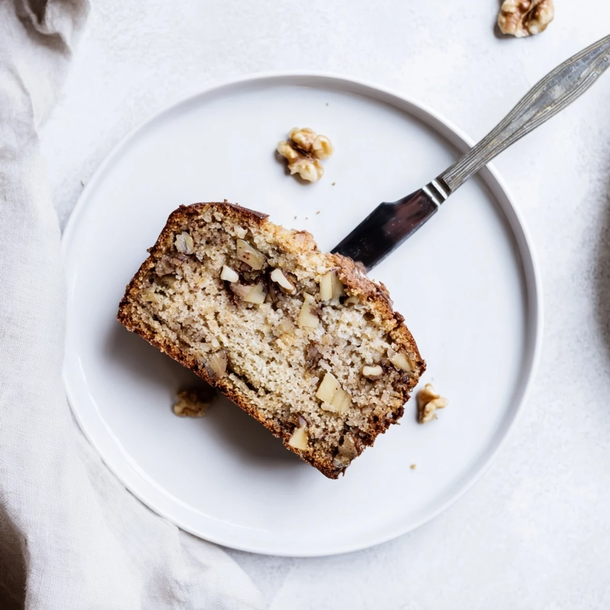 Thick slice of banana nut bread revealing tender crumb and scattered toasted walnut pieces.