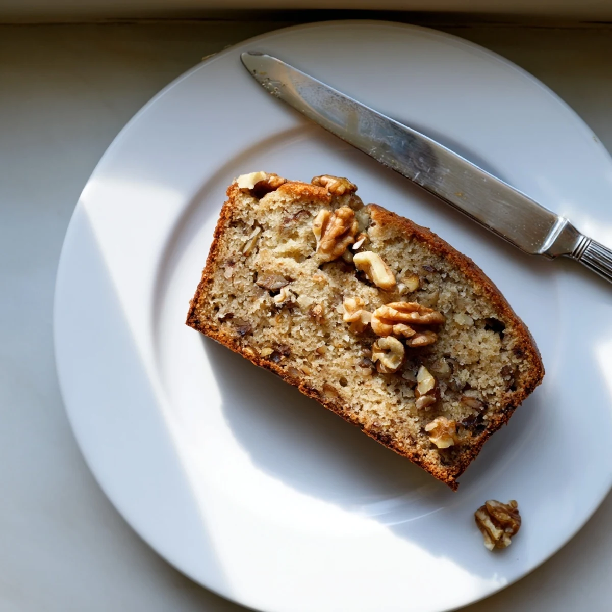Warm slice of moist banana nut bread drizzled with butter beside a steaming mug.