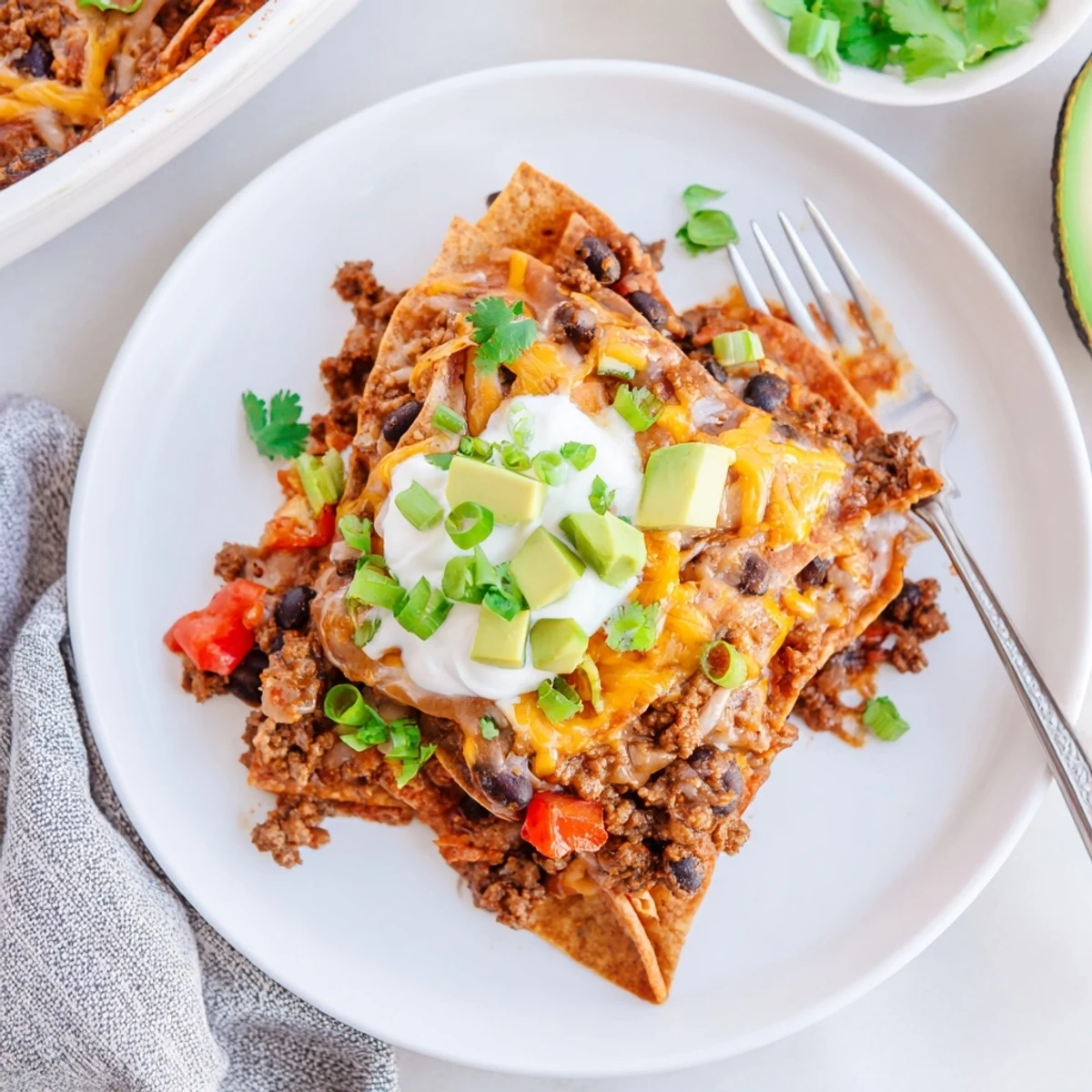 Beef Skillet Enchiladas topped with avocado, sour cream, and golden broiled cheese.