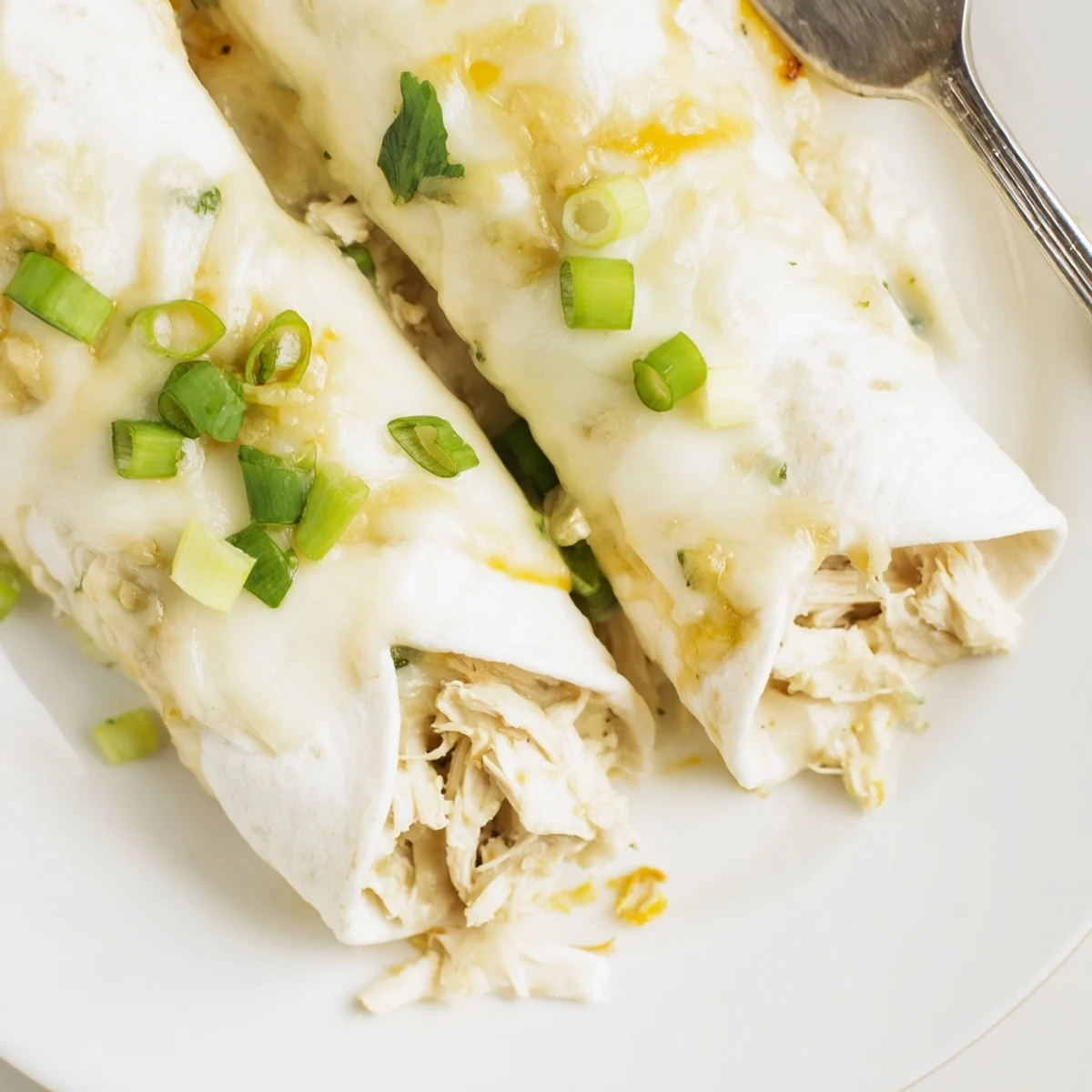 Creamy White Chicken Enchiladas bubbling in a casserole dish, golden cheese topping.