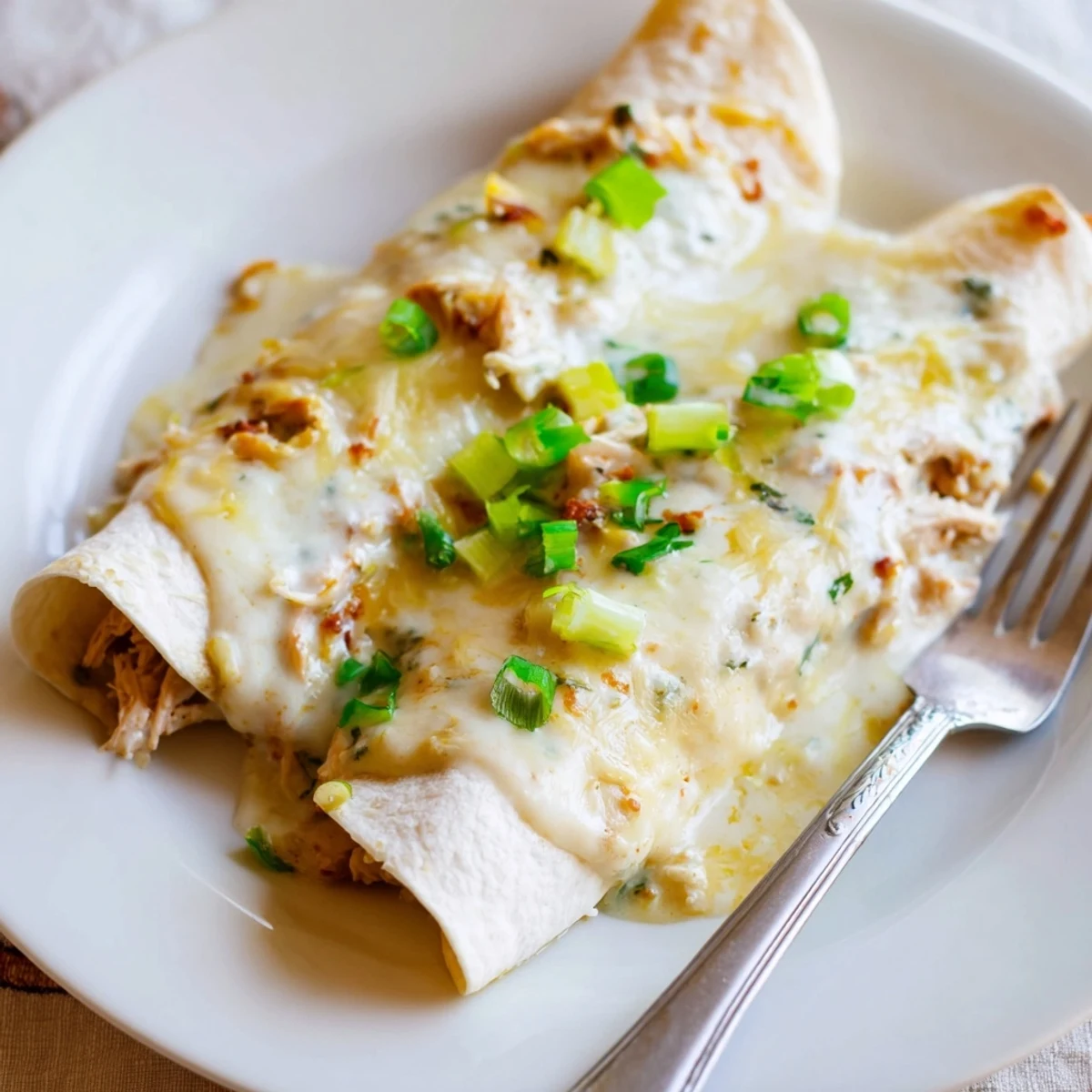 A plate of Creamy White Chicken Enchiladas garnished with cilantro and green onions.