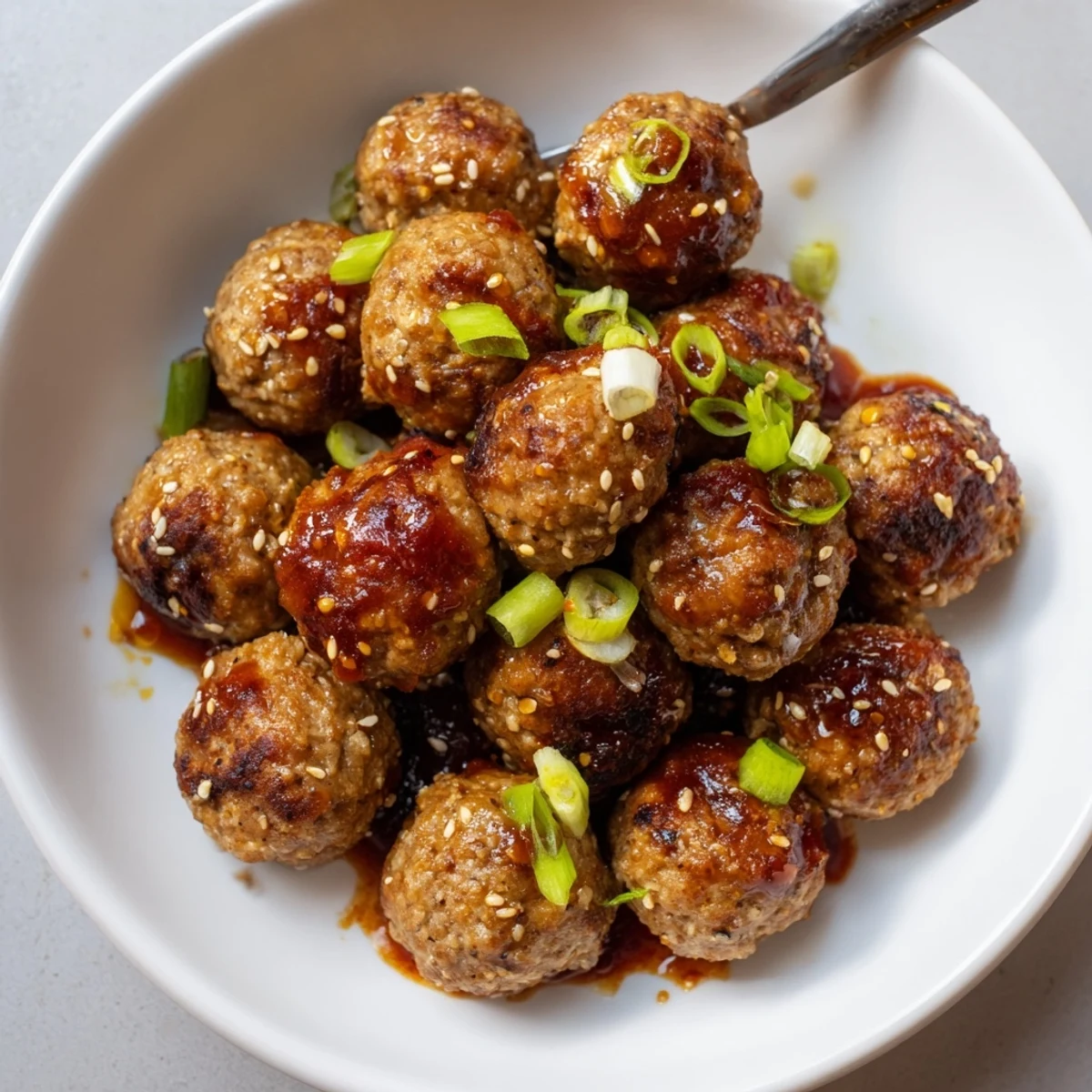 Firecracker Meatballs glazed in glossy spicy-sweet sauce, sprinkled with sesame seeds.