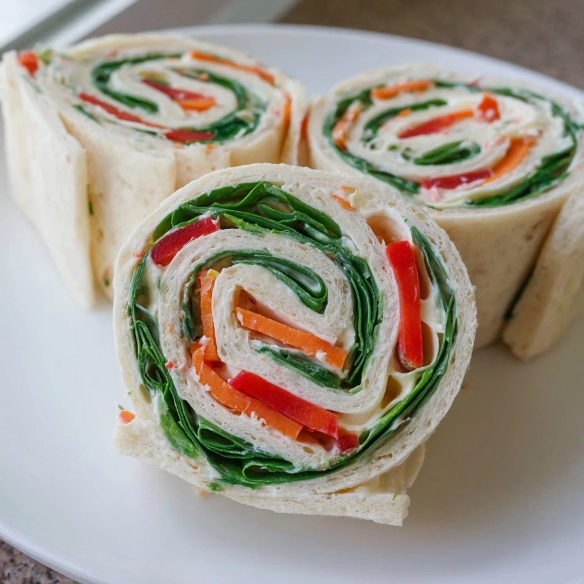 Pinwheel Sandwiches arranged on platter, colorful veggies and creamy cheese visible