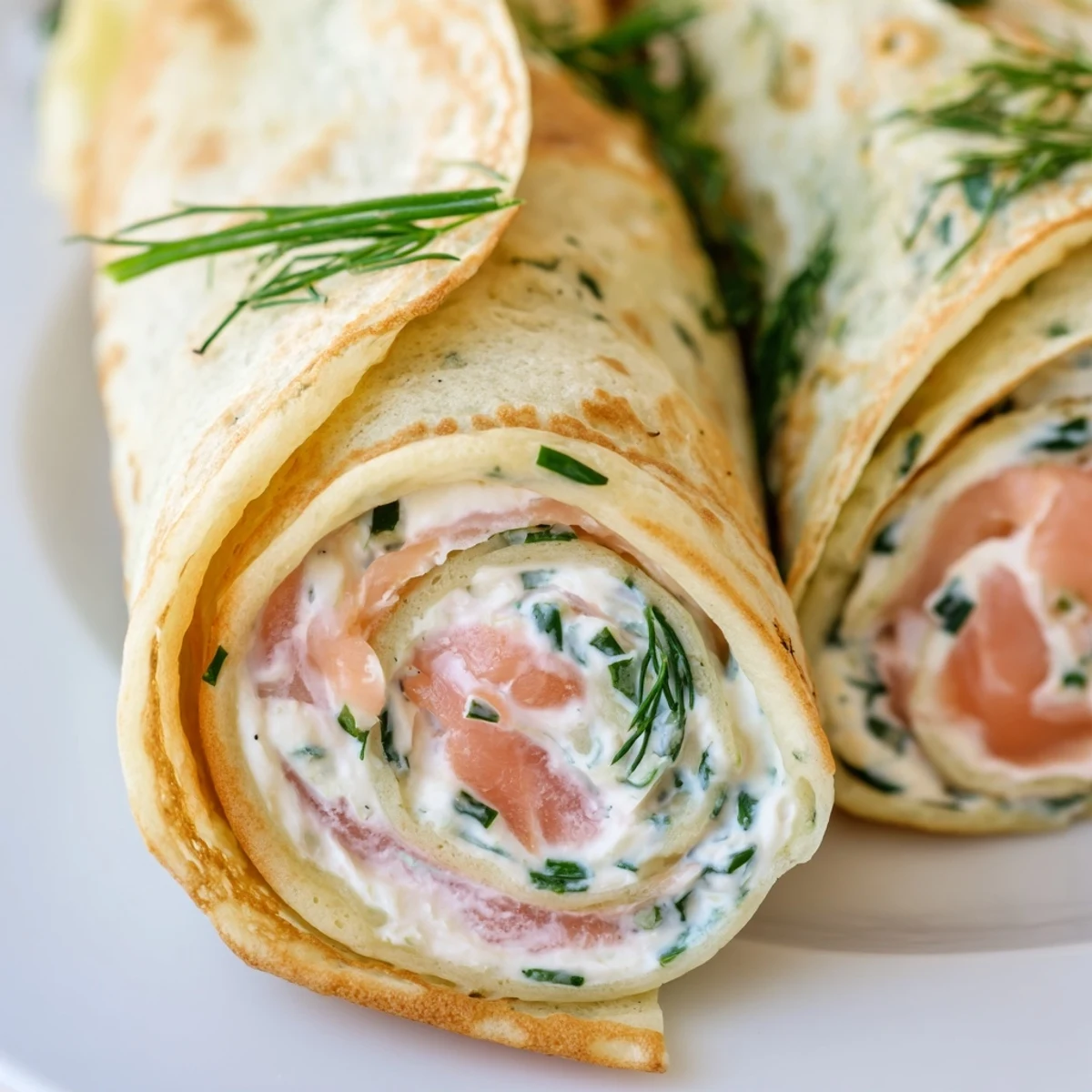 Golden rolled crepes filled with creamy herbed cheese and slices of pink smoked salmon garnished with fresh dill