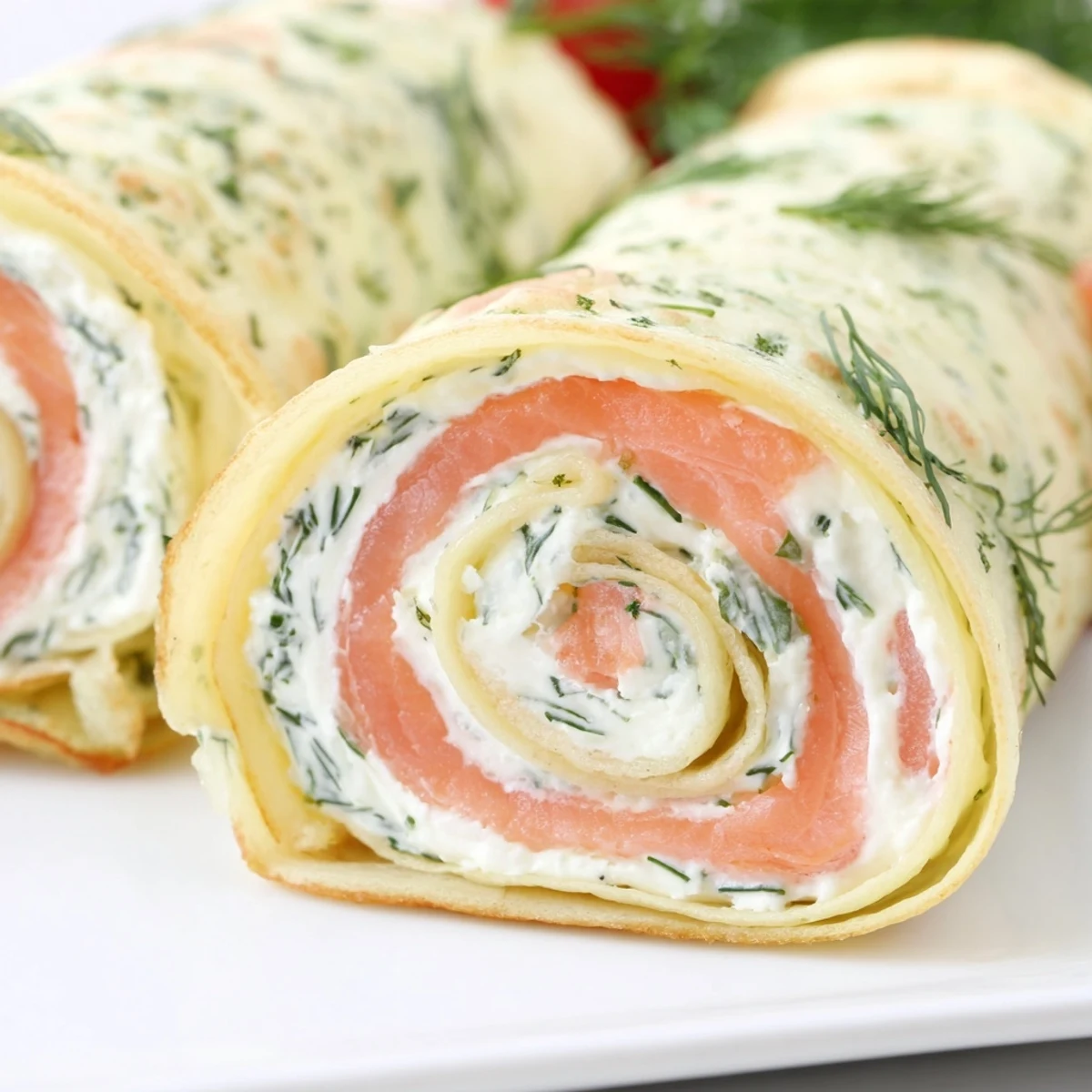 Elegant brunch plate featuring smoked salmon crepes with lemon wedges and sprinkle of green herbs on white platter