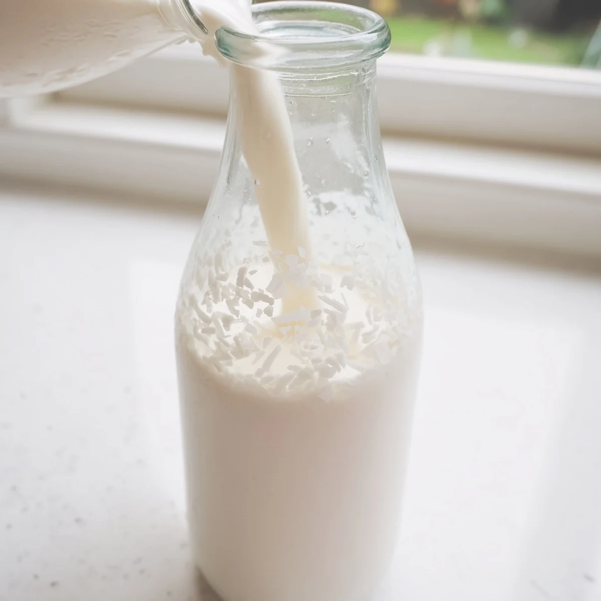 Fresh homemade coconut milk in glass bottle beside shredded coconut and blender