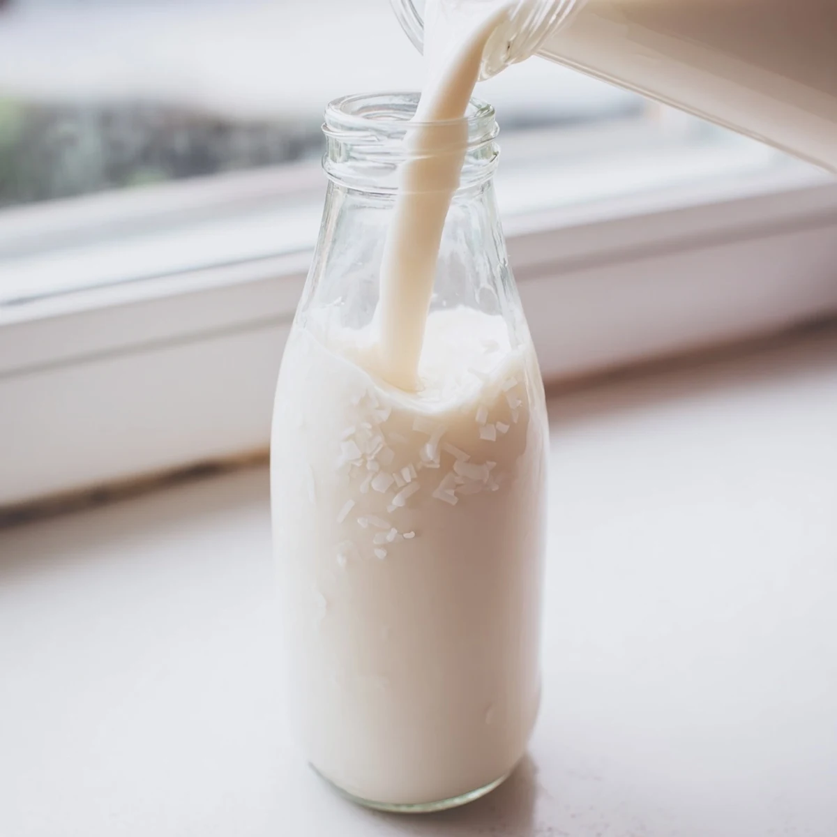 Rich homemade coconut milk in glass pitcher with coconut flakes and kitchen cloth