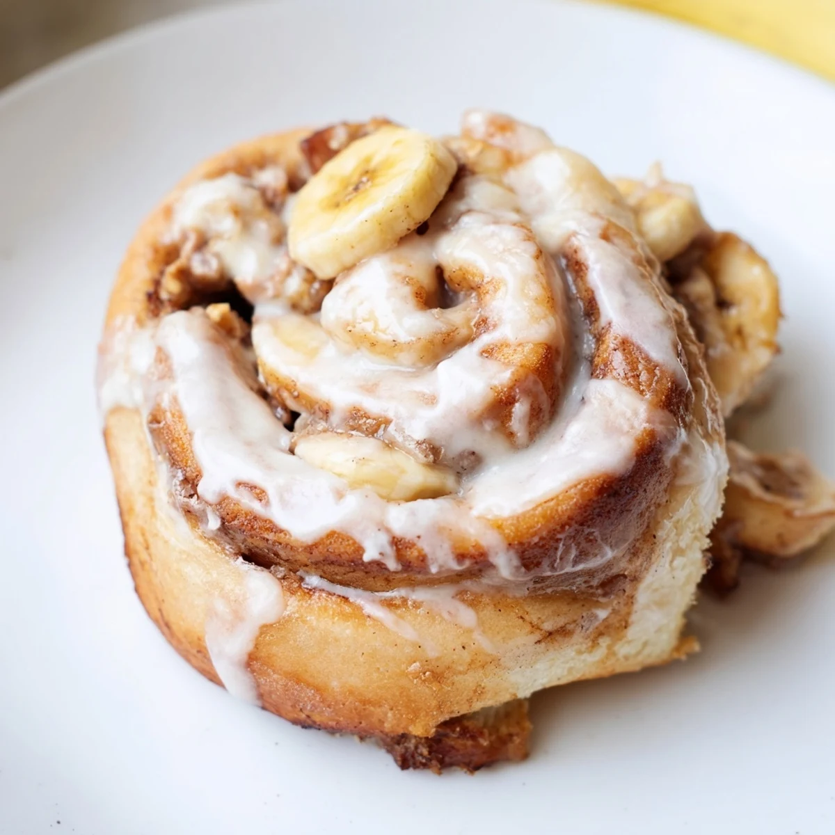 Soft warm banana cinnamon rolls topped with sweet cream cheese frosting on a plate