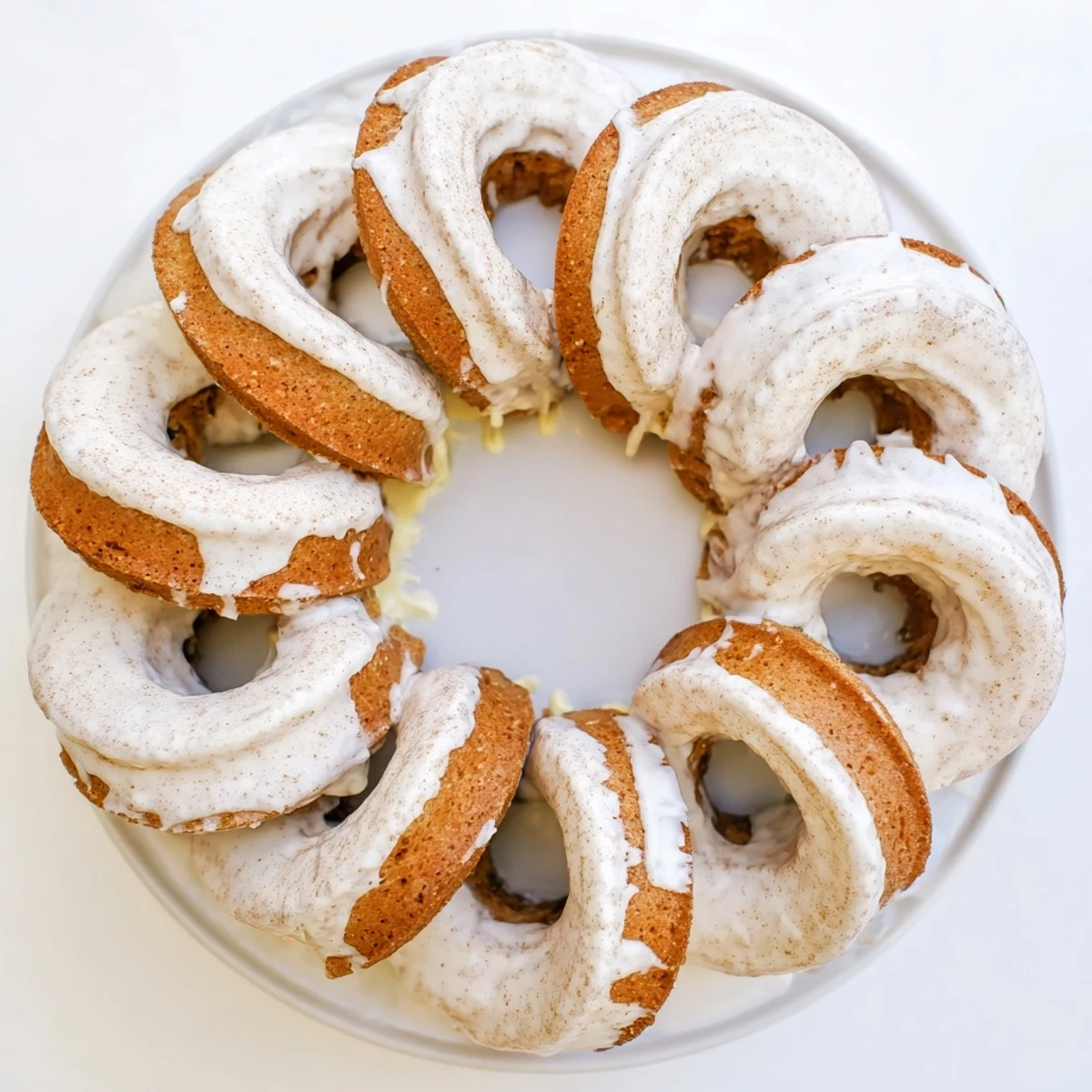 Golden banana bread donuts topped with white glaze on a wire rack