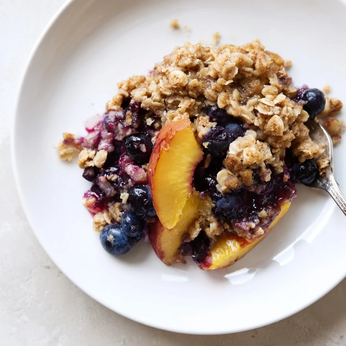 Warm Blueberry Peach Crumble with golden oat topping bubbling, served with ice cream