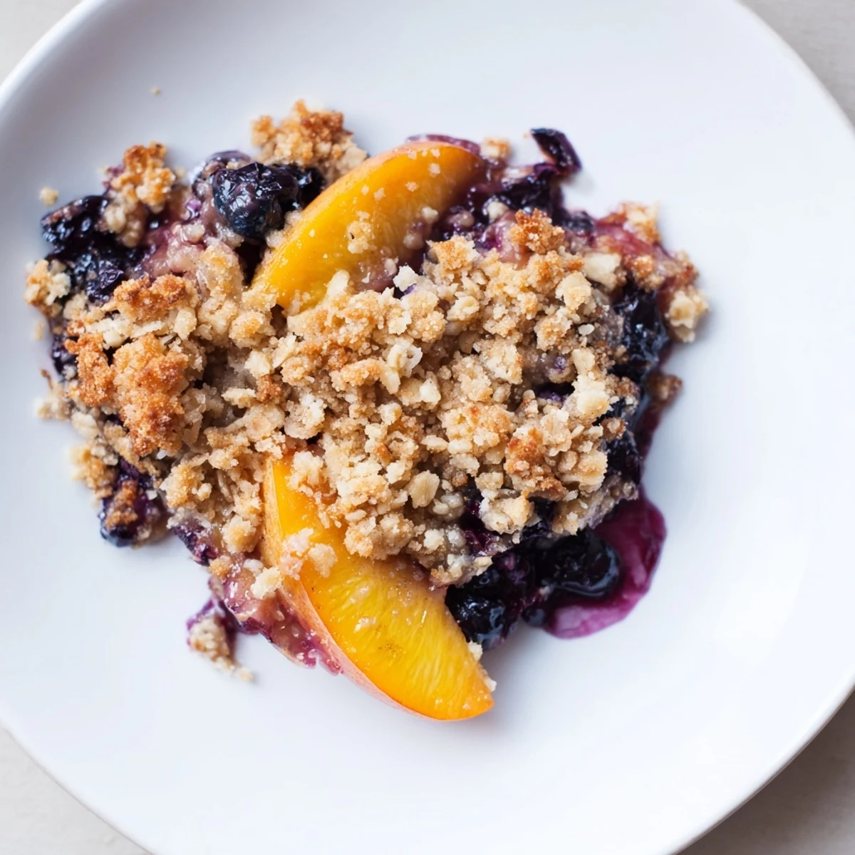 Spoonful of Blueberry Peach Crumble steaming warm, buttery topping and tart berries