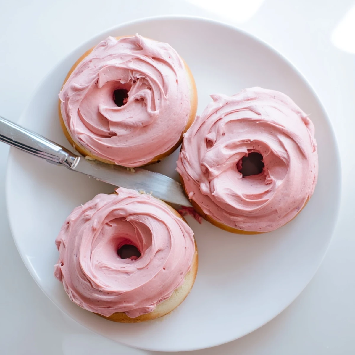 Pink strawberry buttercream frosted donuts arranged on a cooling rack with sprinkles