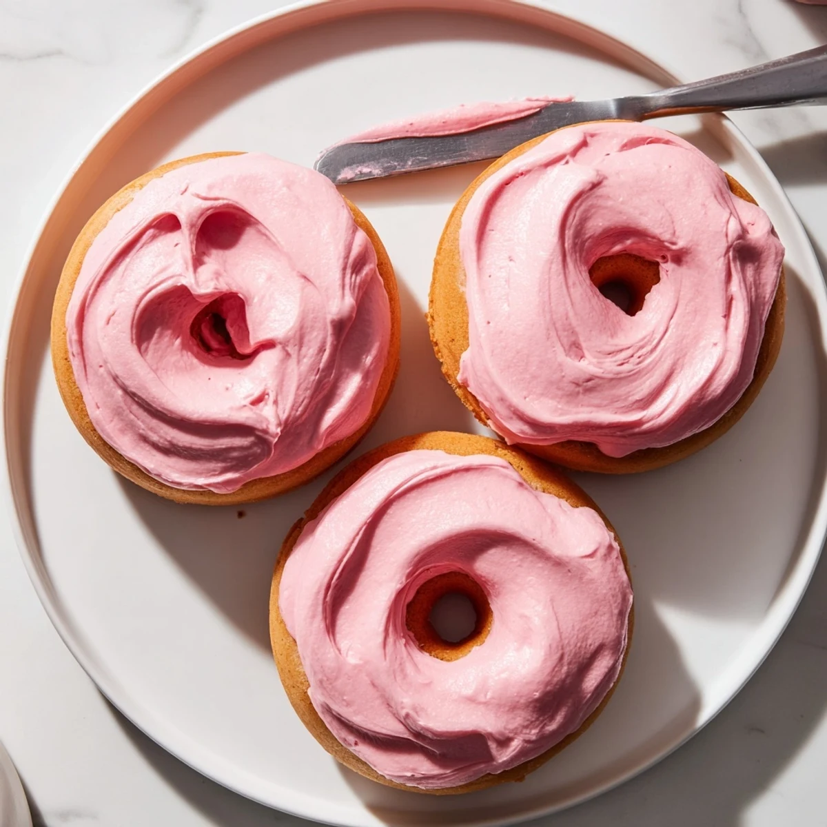 Golden baked donuts topped with fluffy strawberry buttercream frosting and fresh berries